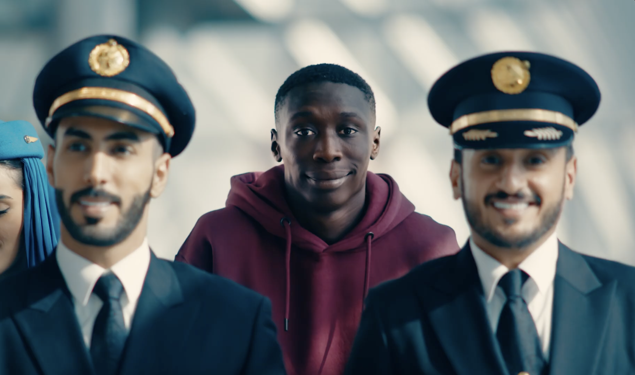 A young man in a maroon hoodie standing between two uniformed pilots with black hats, all smiling.