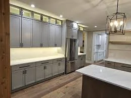 Modern kitchen with gray cabinets, stainless steel appliances, a white island, and wooden flooring.