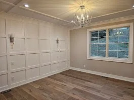 Empty room with white paneled walls, hardwood floors, a window, and a chandelier
