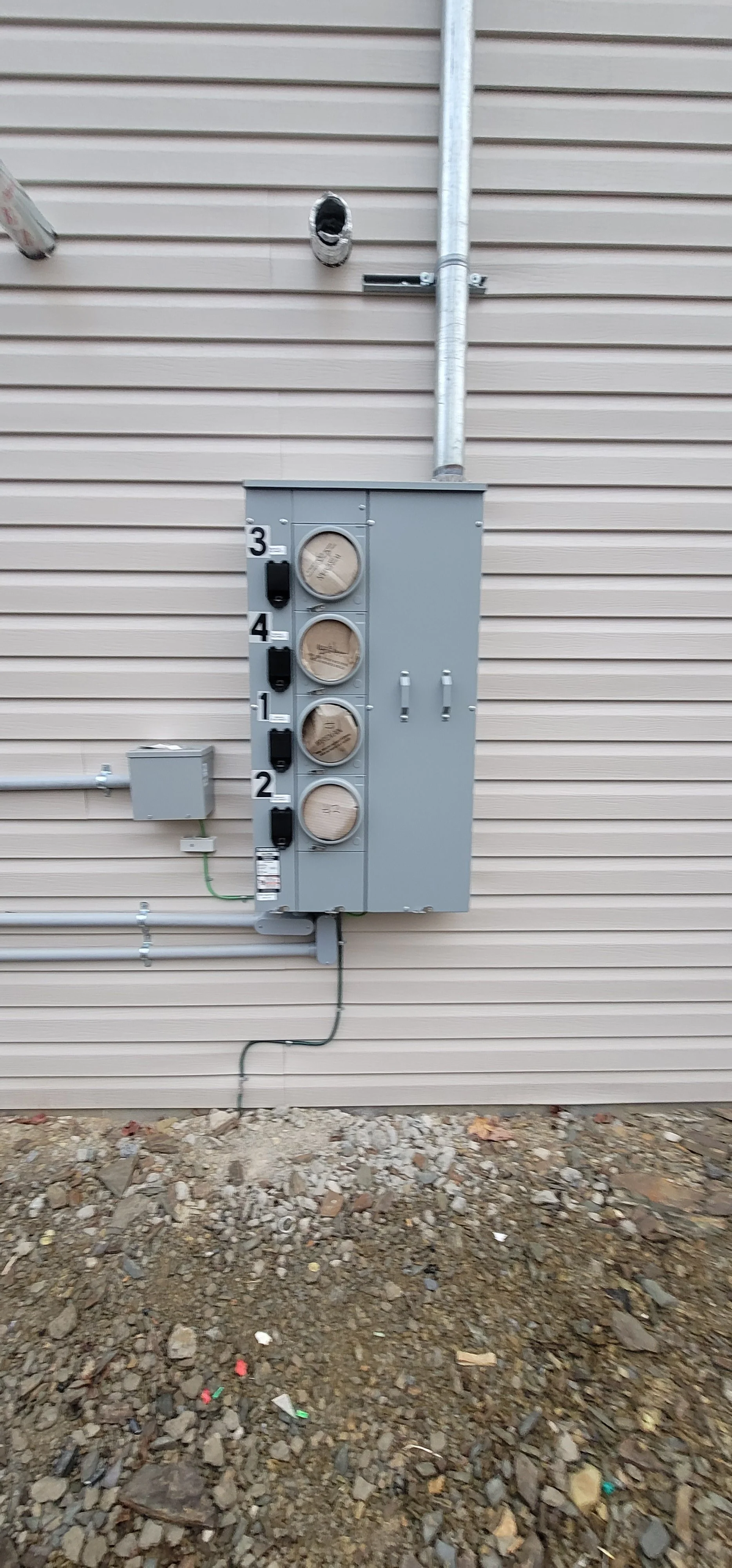 Electrical meter box and circuit breakers mounted on the exterior beige siding of a building. The house number 314 is visible on the panel.