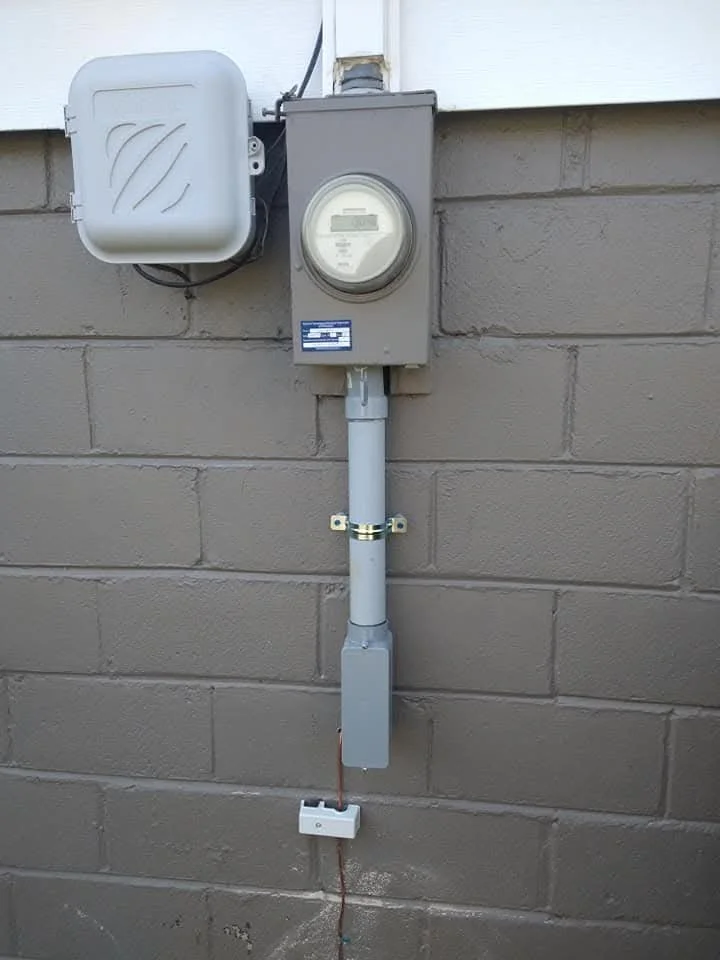 Outdoor electric meter box and electrical box mounted on a gray brick wall with conduit piping.