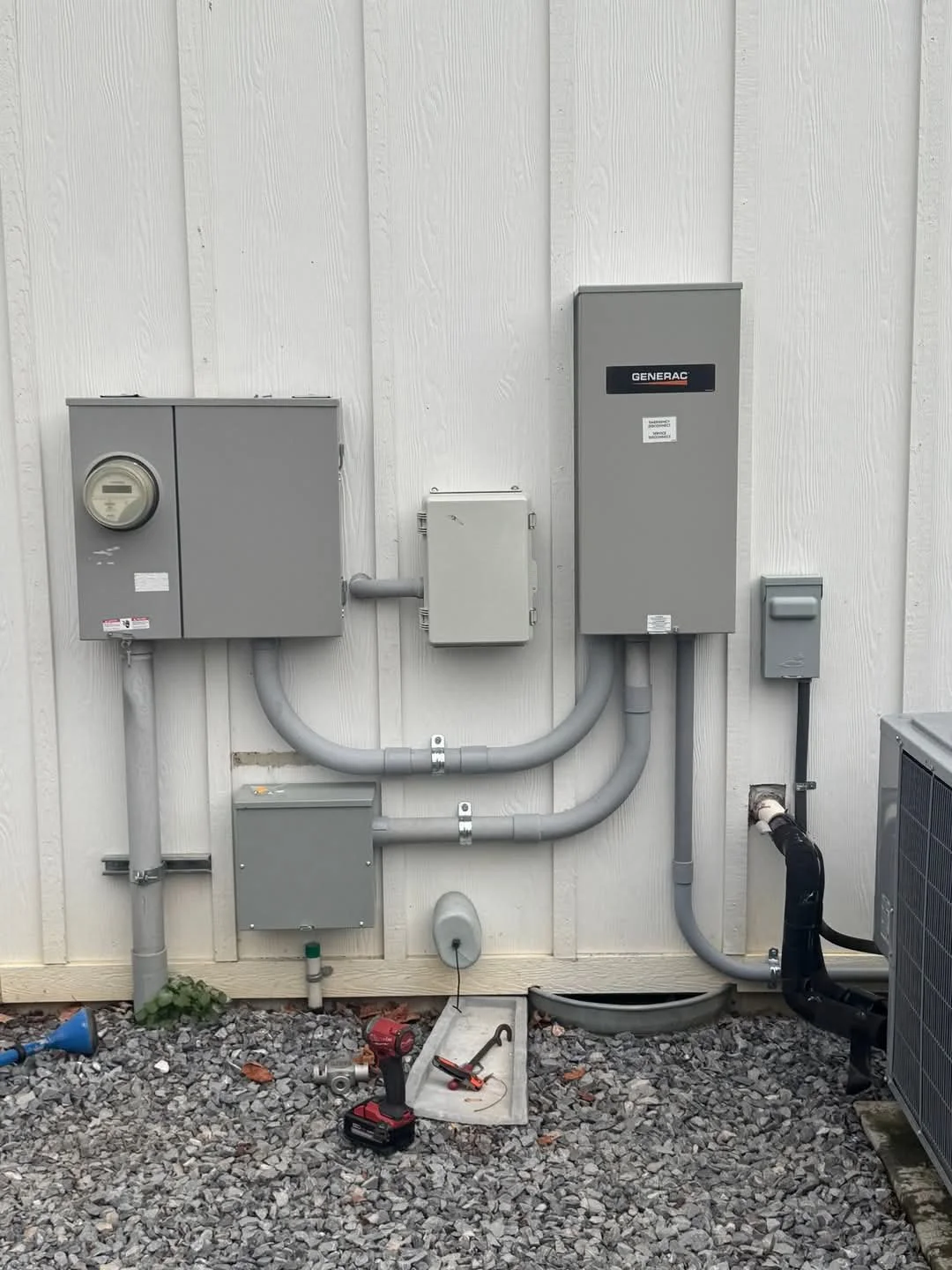 Outdoor electrical and generator panels with tools on gravel ground.