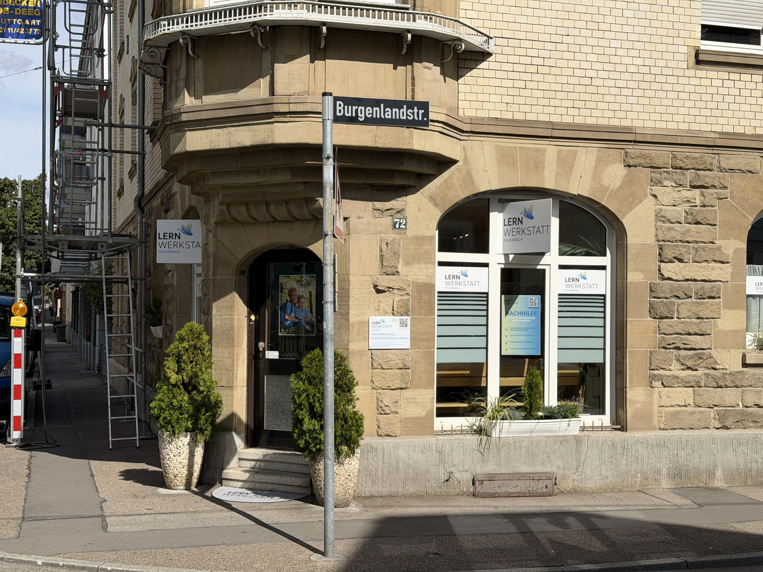Straßenschild mit der Aufschrift 'Burgenlandstr.' vor einem historischen Gebäude mit LERN WERKSTATT Schild und großen Fenstern.