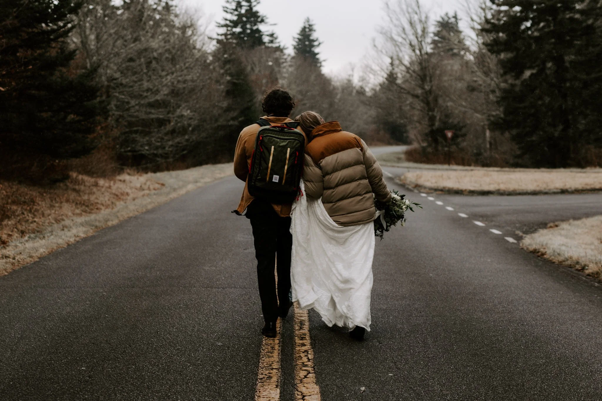 Bride and groom walk arm in arm down the middle of the road in a snowy national forest