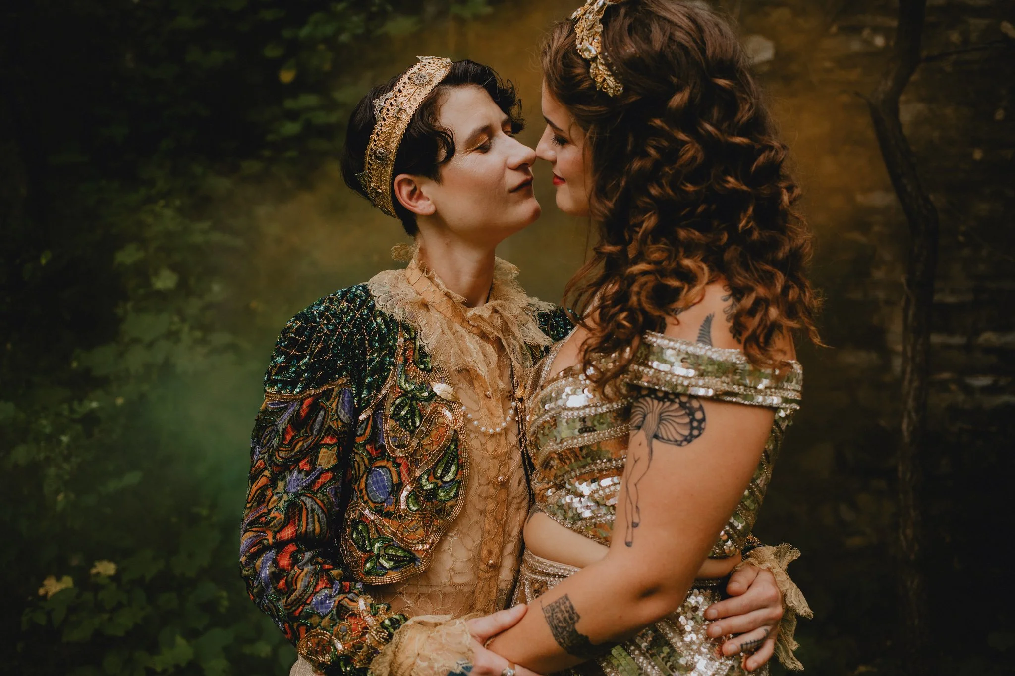 Wedding couple lean in for a kiss, in their golden attire, with green and orange smoke bombs behind them