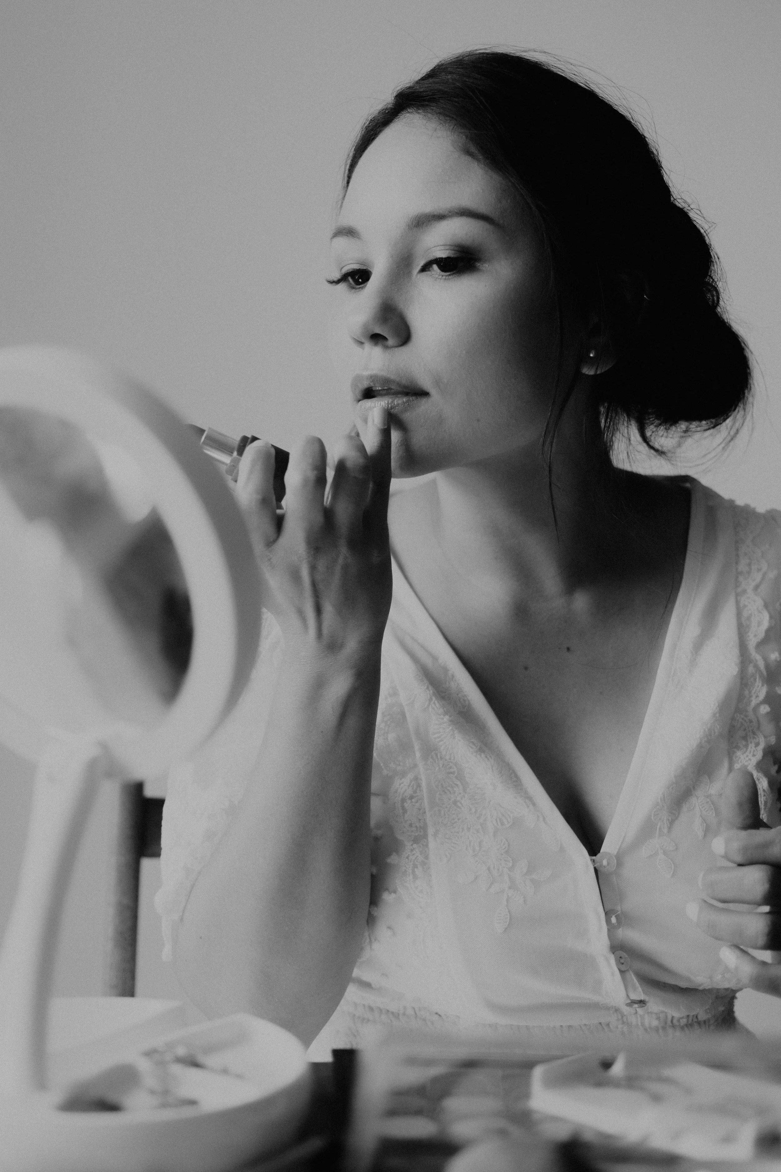 Bride uses her pink to softer her lipstick while looking into a small mirror