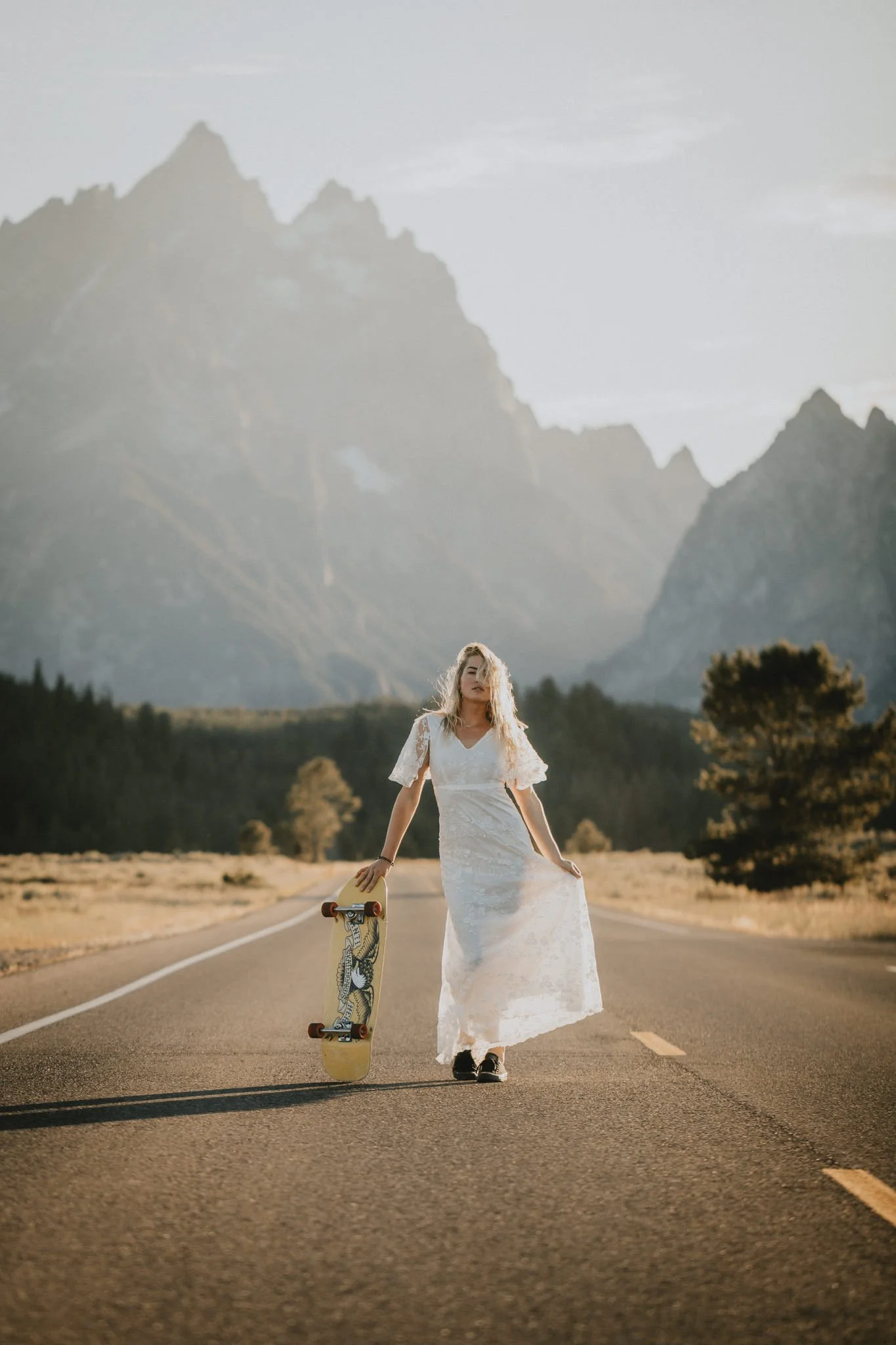 Bride stands with her skateboard on the road leading into Grand Teton National Park
