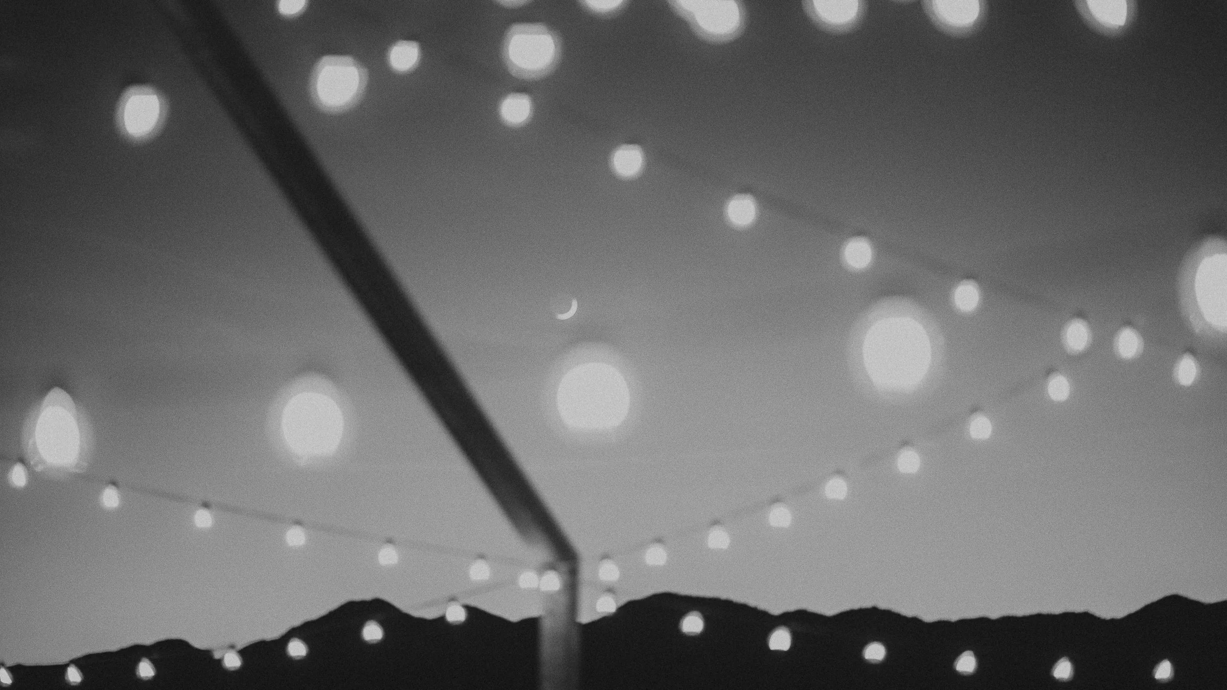 ruin venue with cafe lights under a crescent moon with shadowed foothills in the distance
