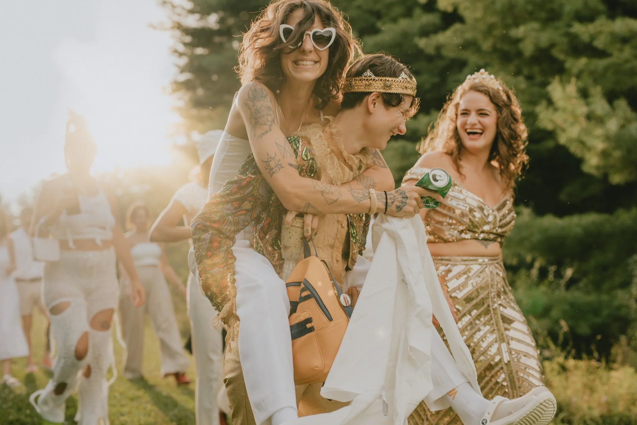 Two brides walk away from their ceremony, giving a piggyback ride to a friend