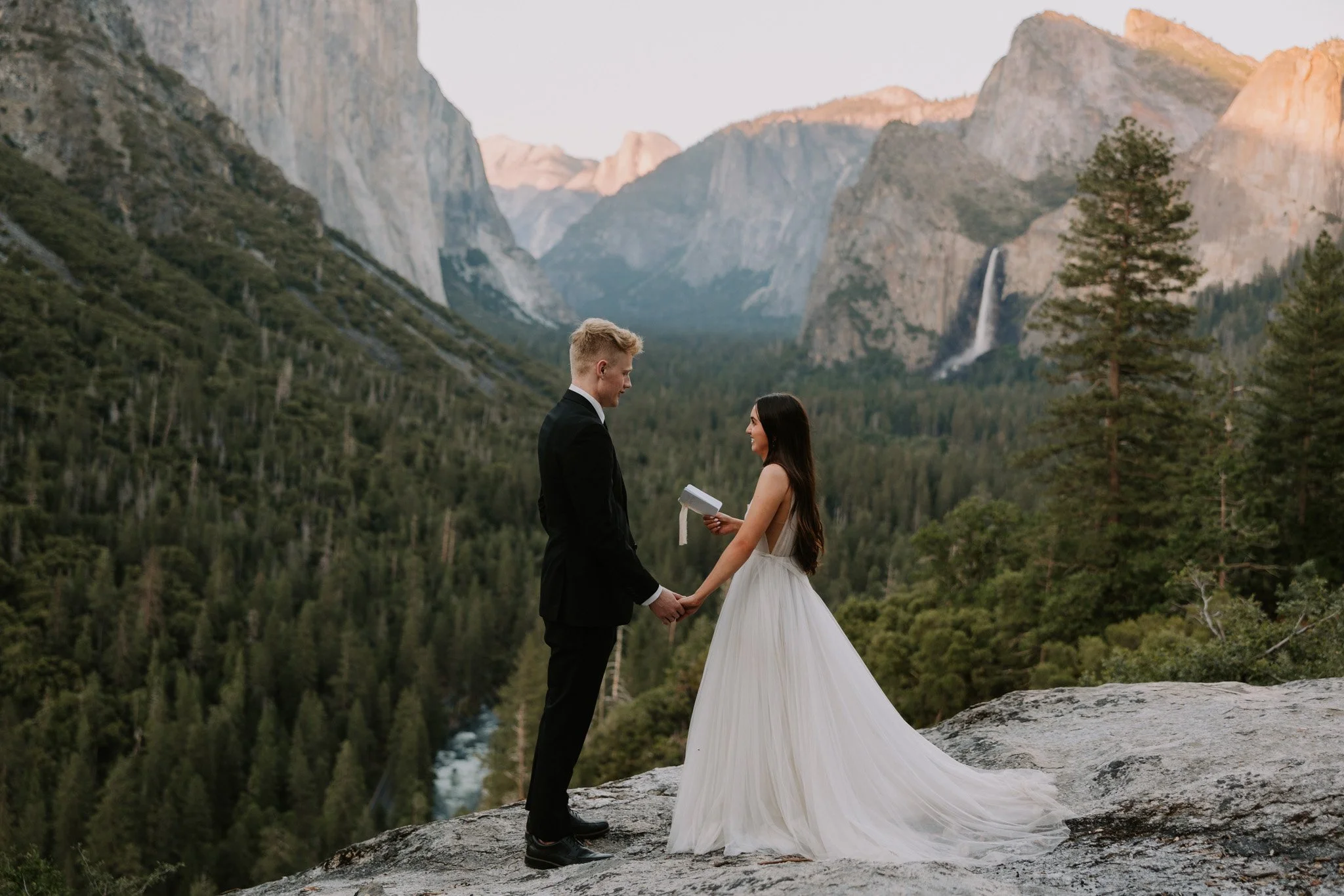 An elopement couple share their vows in Yosemite on a rocky ledge with Valley View in the background