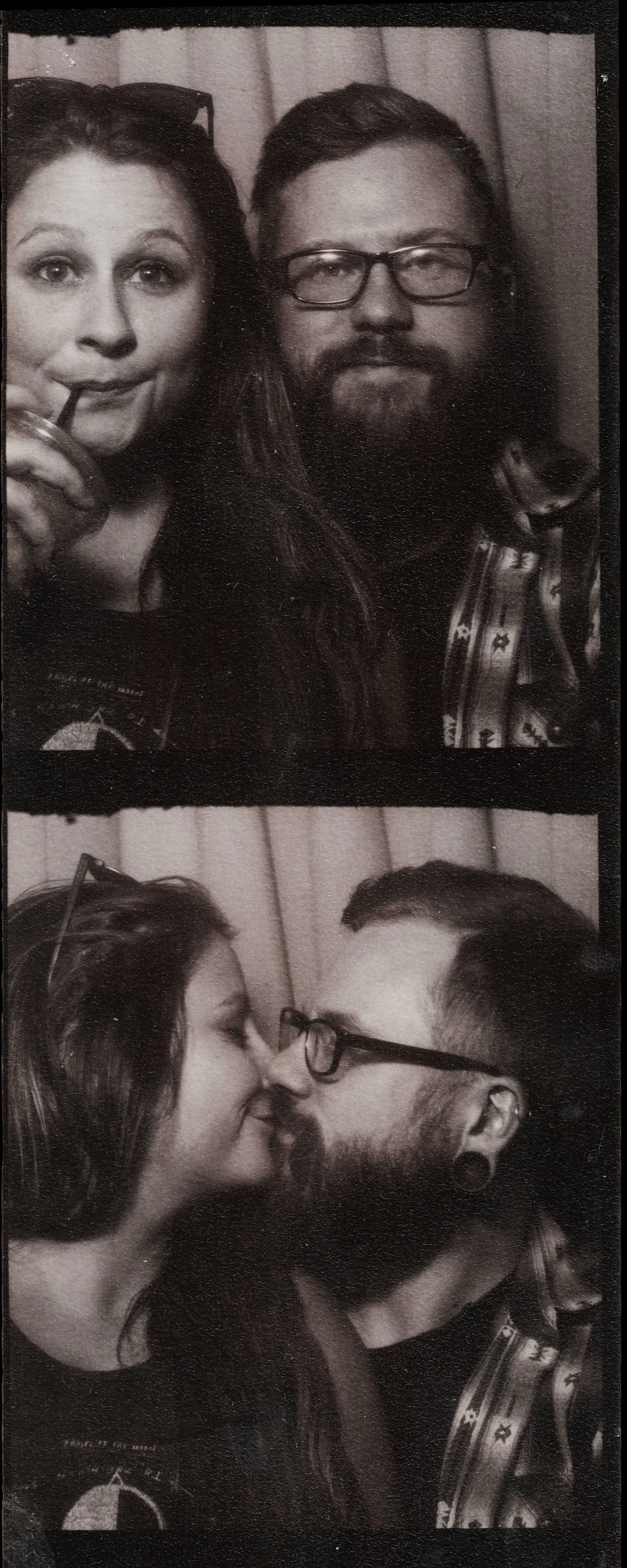 Two black and white photographs showing a couple. In the first photo, they are close, with the woman looking at the camera and sipping a drink through a straw, and the man looking directly ahead with glasses and a beard. In the second photo, they are kissing, with the woman's face in profile and the man’s face turned towards her, still wearing glasses and with a beard.