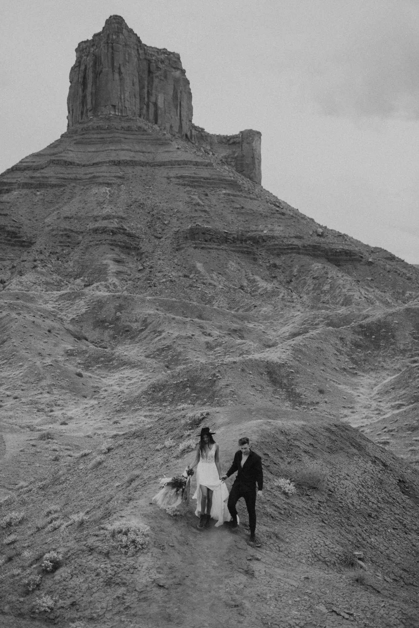Black and white photo of a boho couple celebrating their engagement in Moab, hiking, with a mesa in the background
