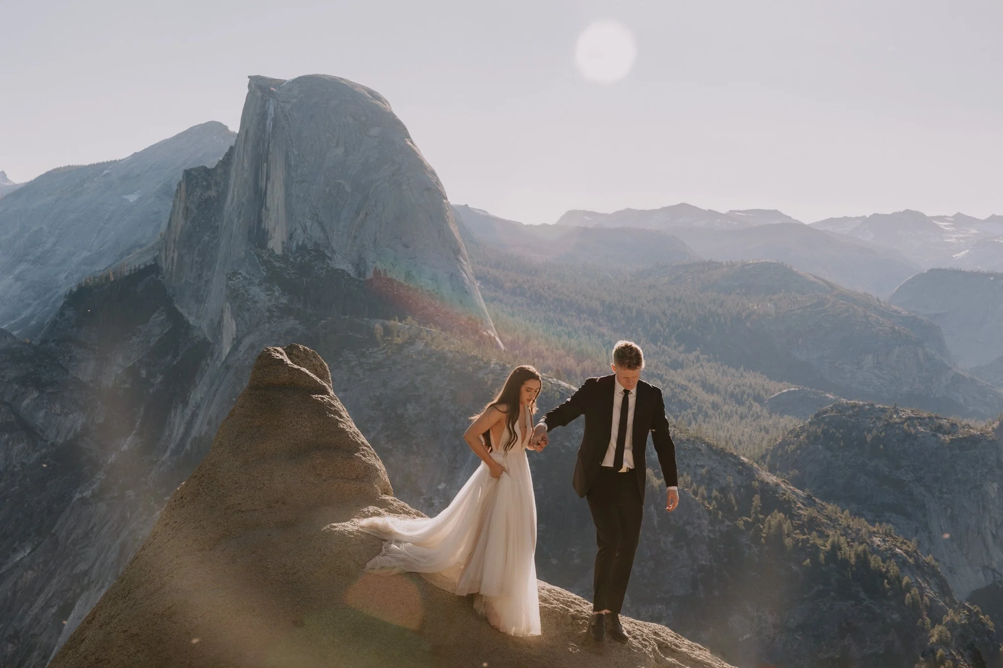 An eloping bride and groom walking at Glacier Point in Yosemite with Half Dome in the background.