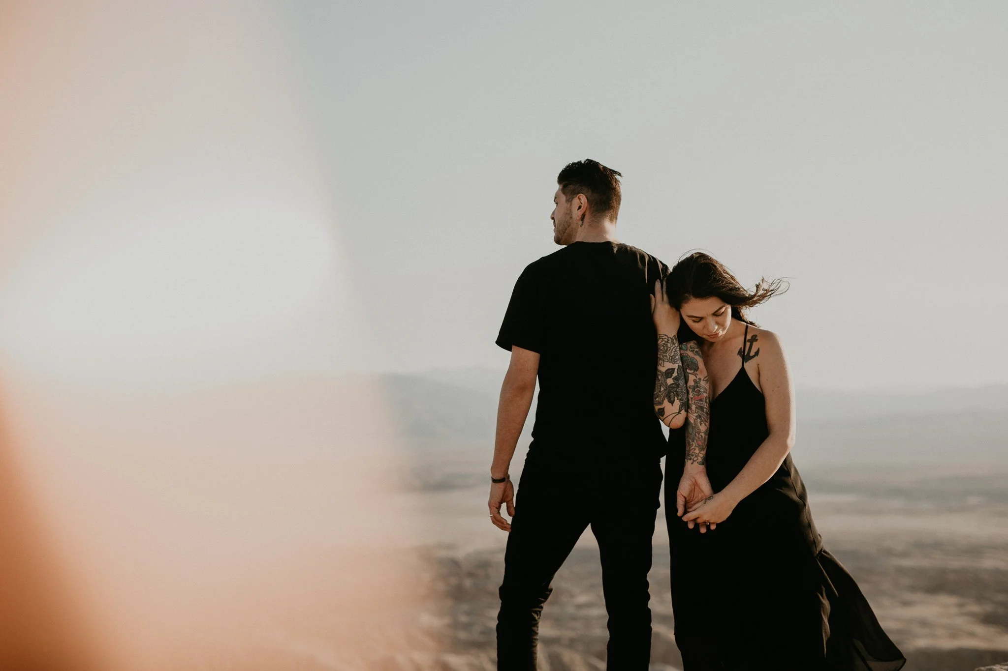 A tattooed couple standing at Anza Borrego during sunset, with the man facing away and the woman looking down, holding hands