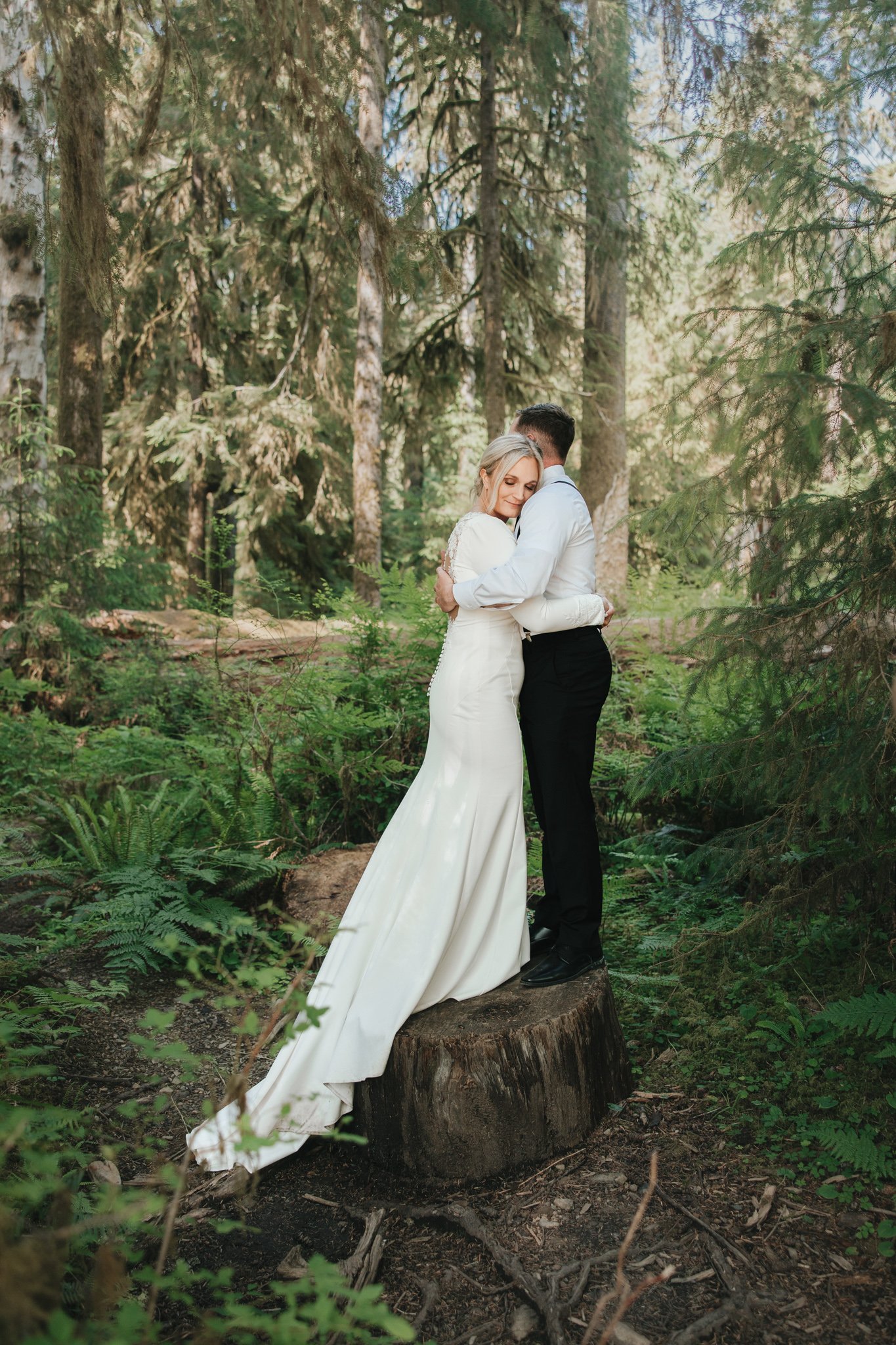 Wedding couple hugs on a downed tree stump while hiking through the Hall of Mosses in the Olympic National Park