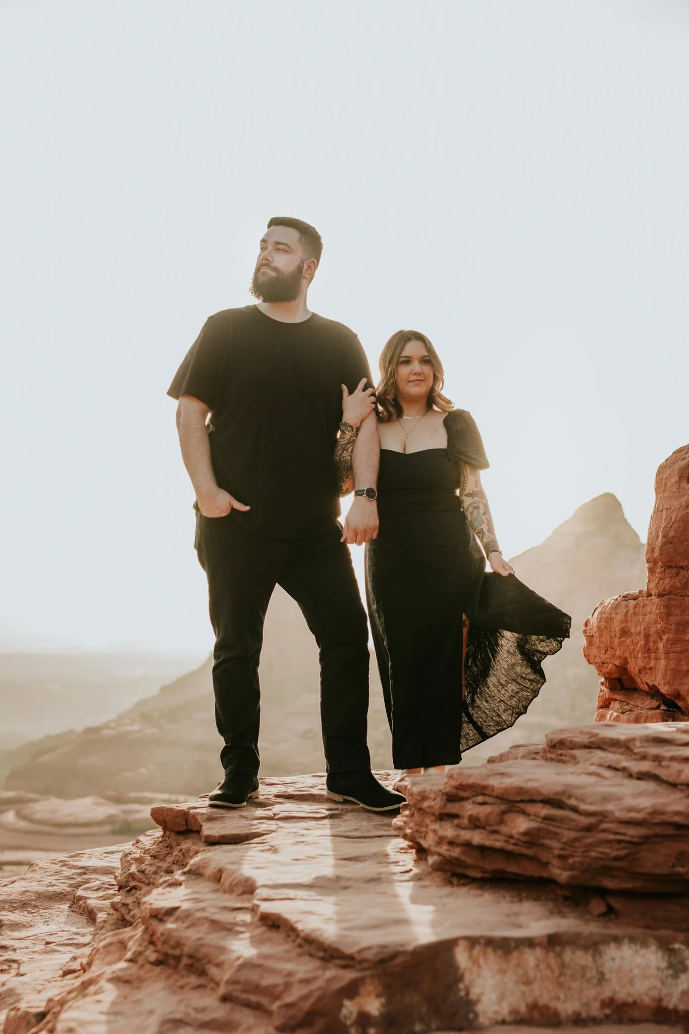 Nontraditional couple stands in all black on a rocky ledge in Sedona at sunset