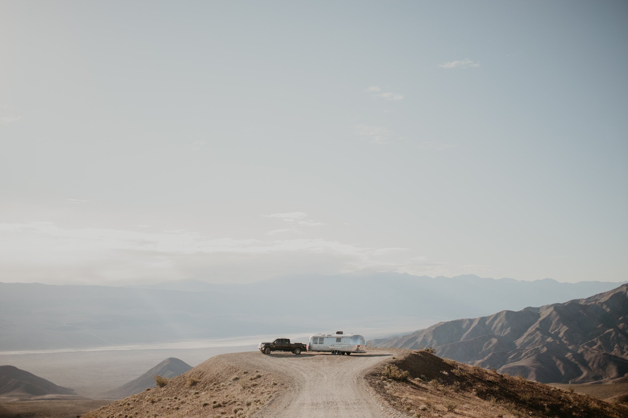 A black pickup truck parked on a dirt road in a desert landscape with mountains in the background, a bright sky above.