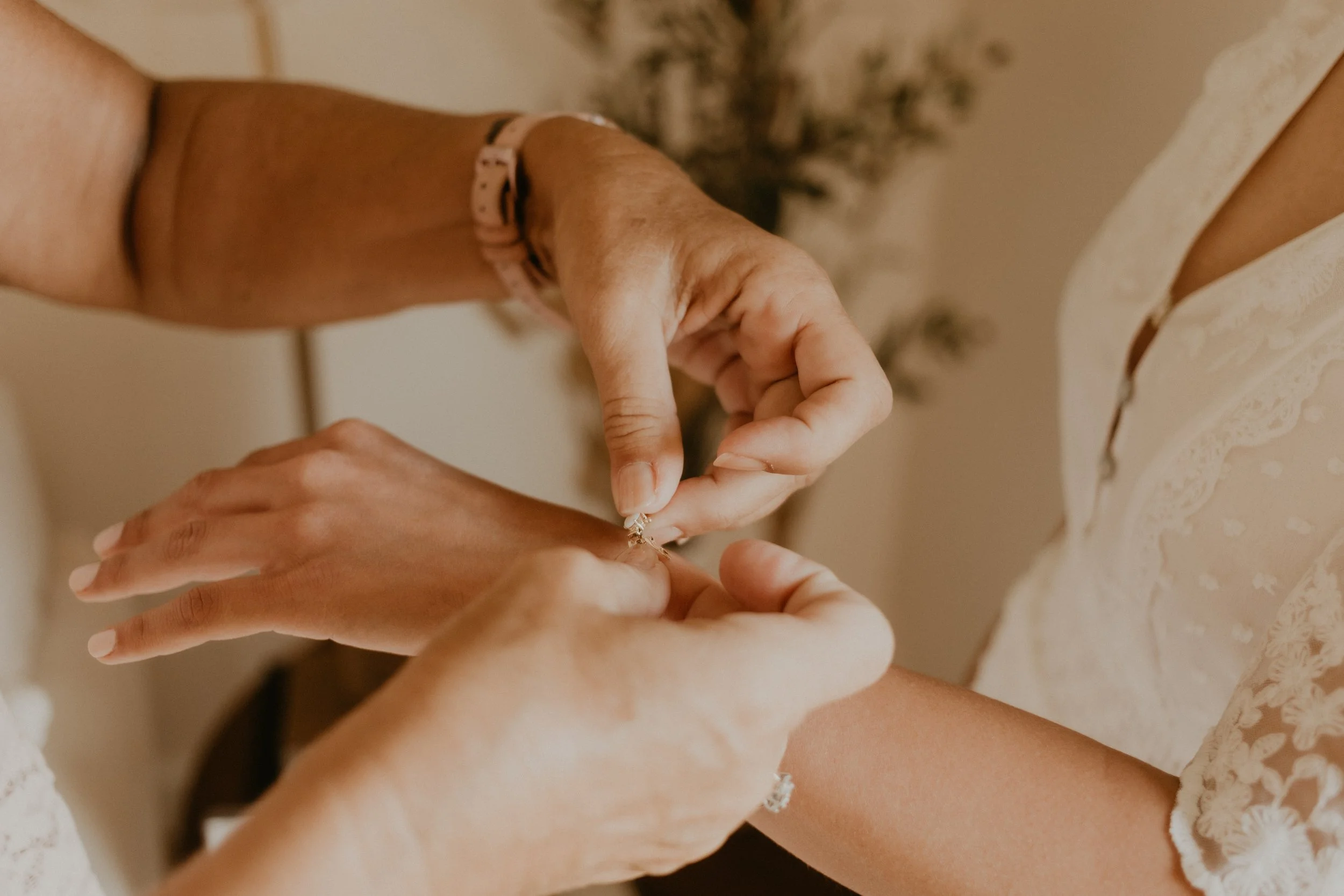 Close up of mother-in-law's hand placing a gifted bracelet on the arm of the bride.