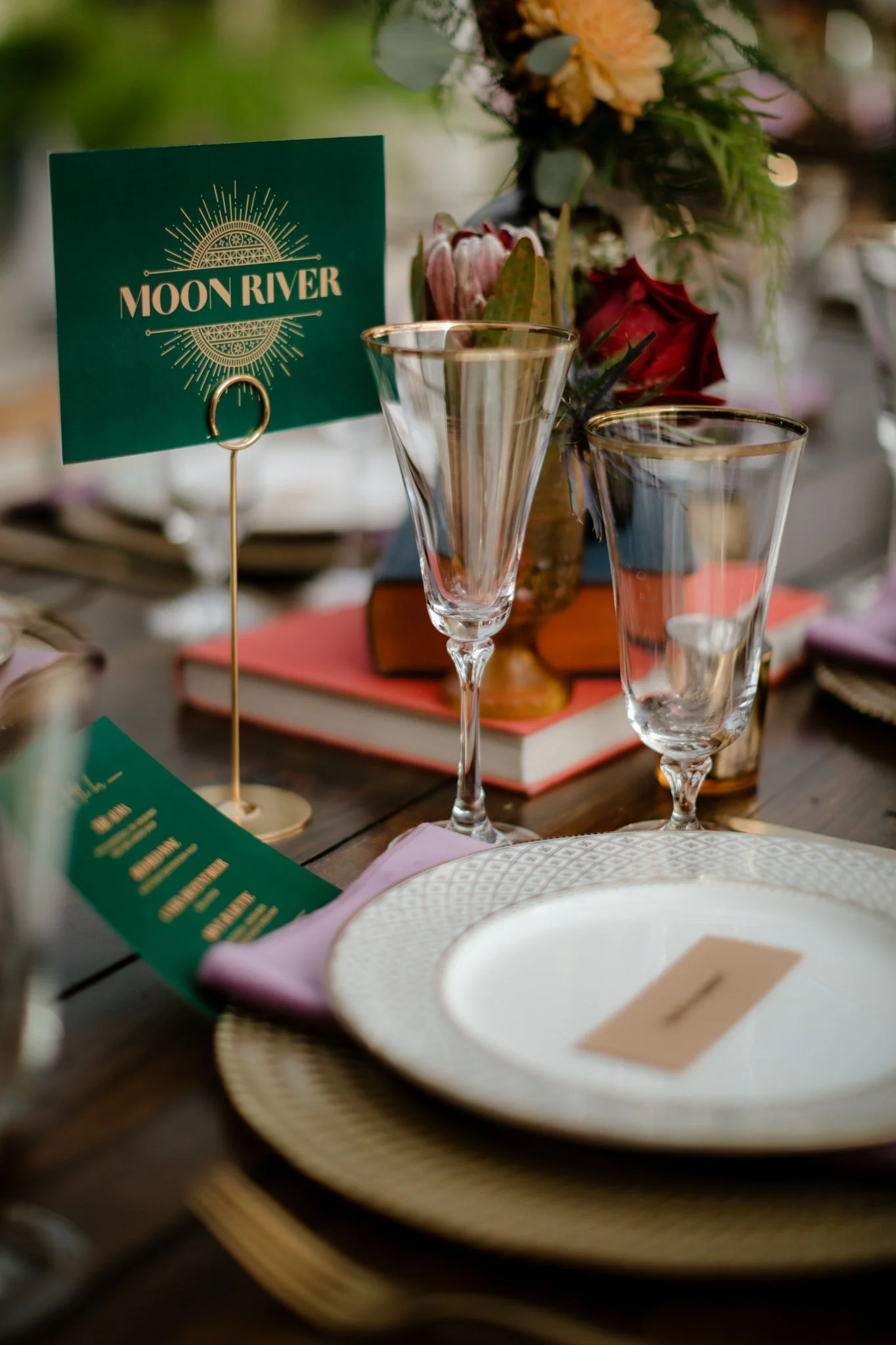 A close up of the tableware and custom table names, showing gold rimmed fluted glasses with white and gold place settings.