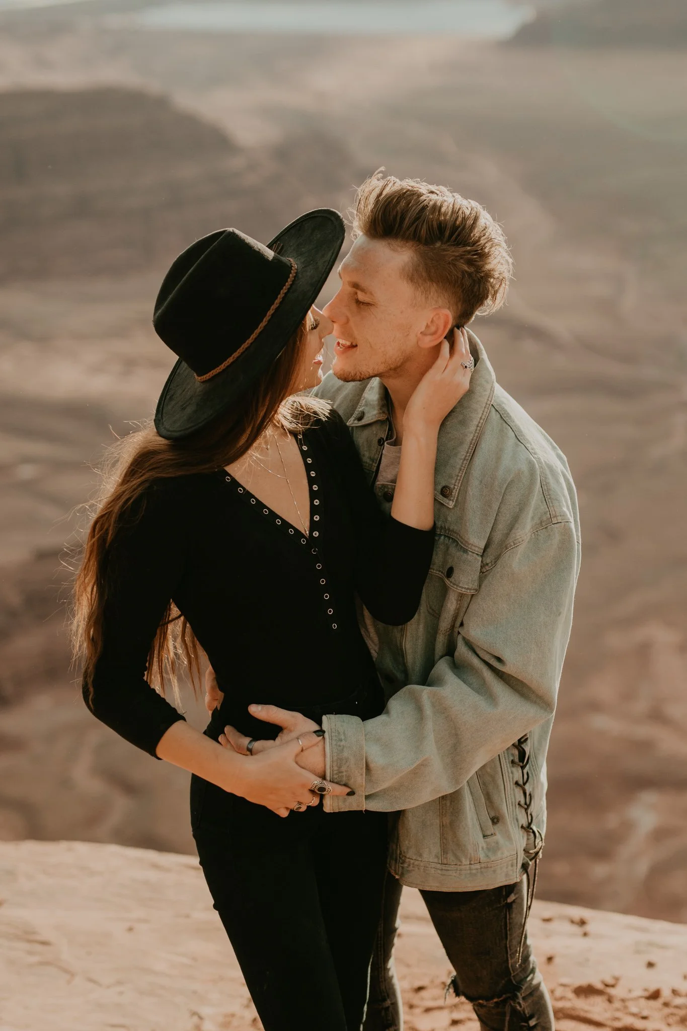 Boho couple get close and embrace as they stand on a cliff in Dead Horse Point State Park