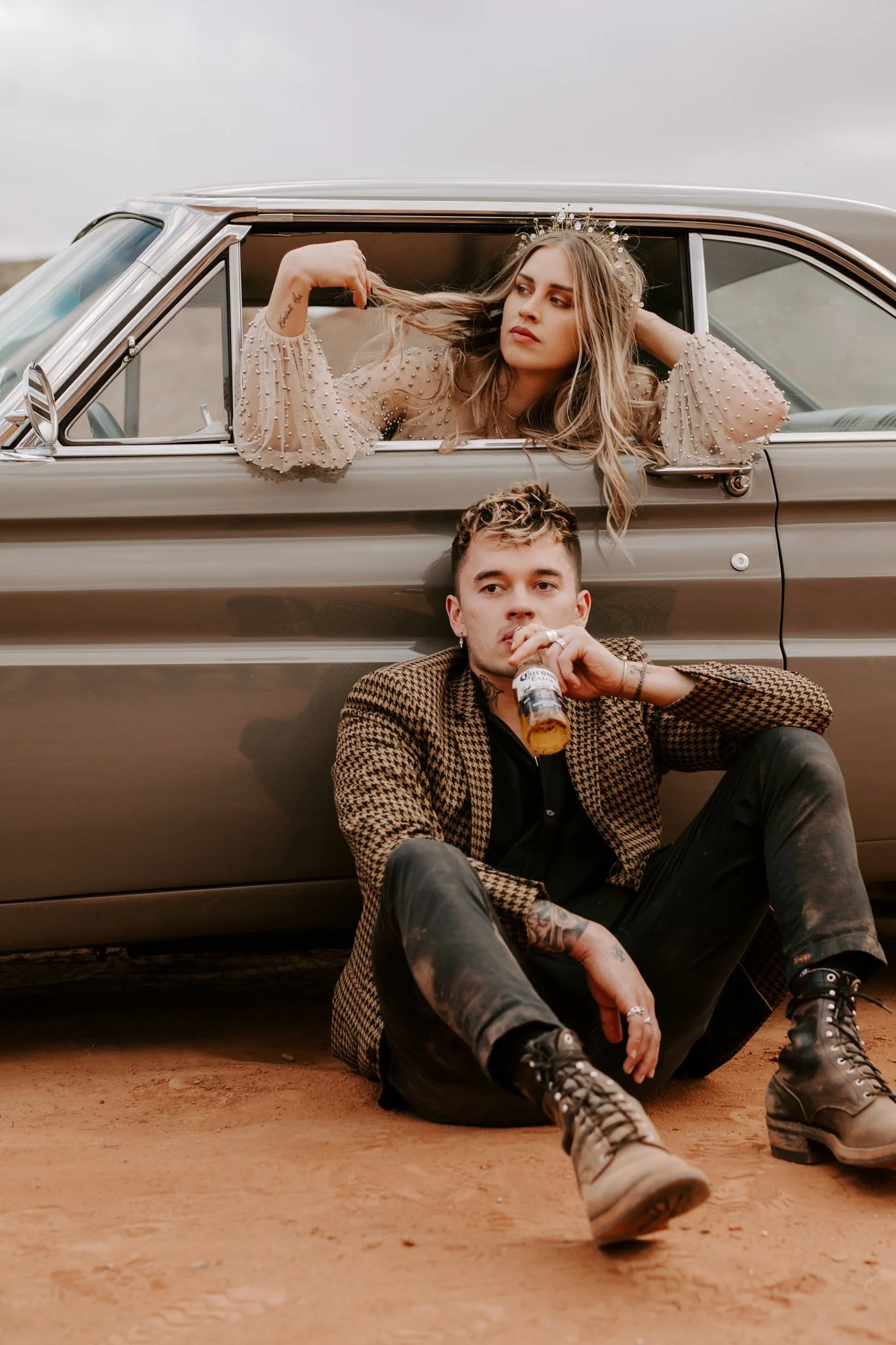 A nontraditional tattooed couple sit against their vintage car during their engagement shoot in Ida Gulch