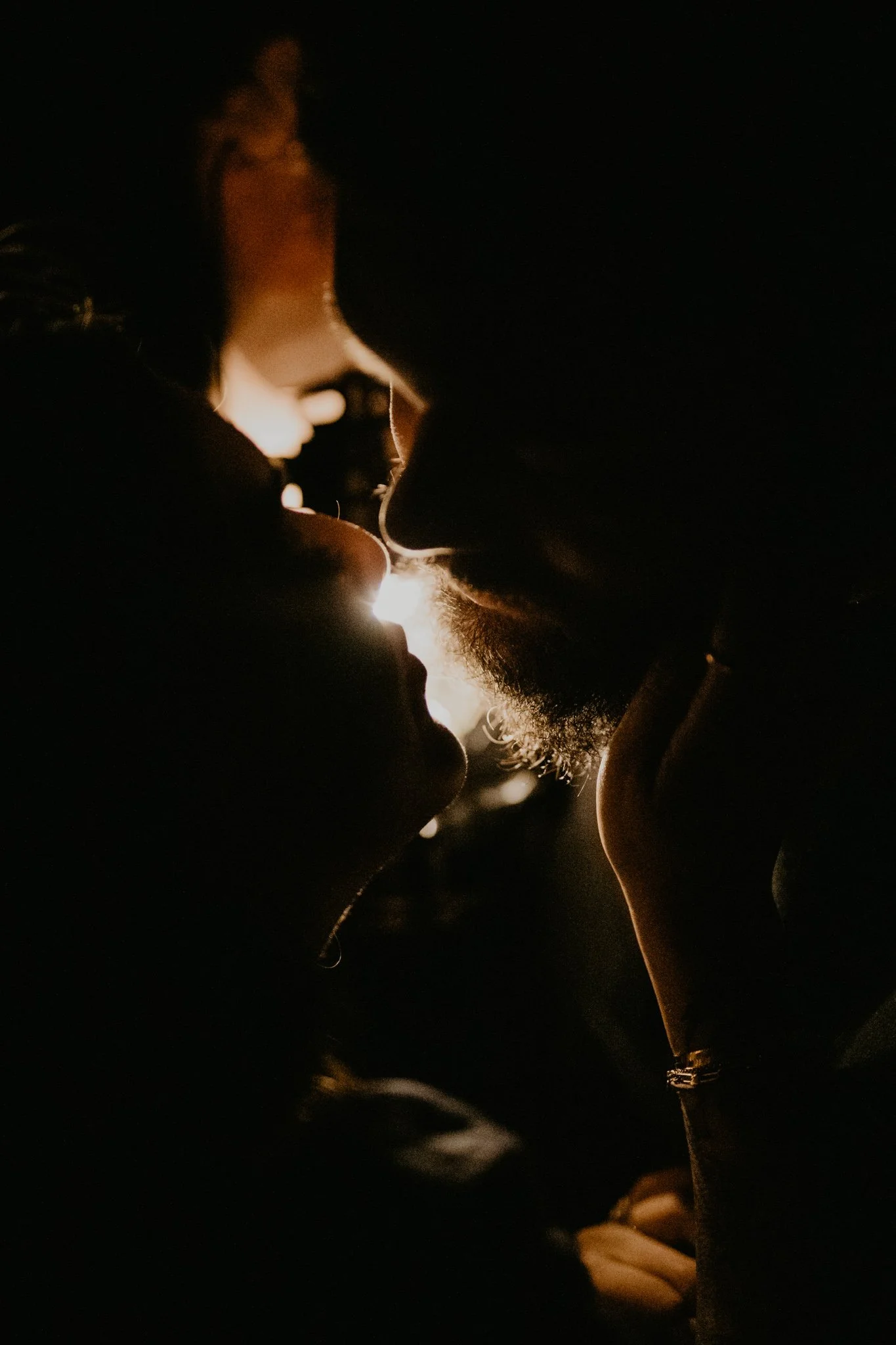 Silhouetted elopement couple kissing at night, backlit by their jeep headlights.