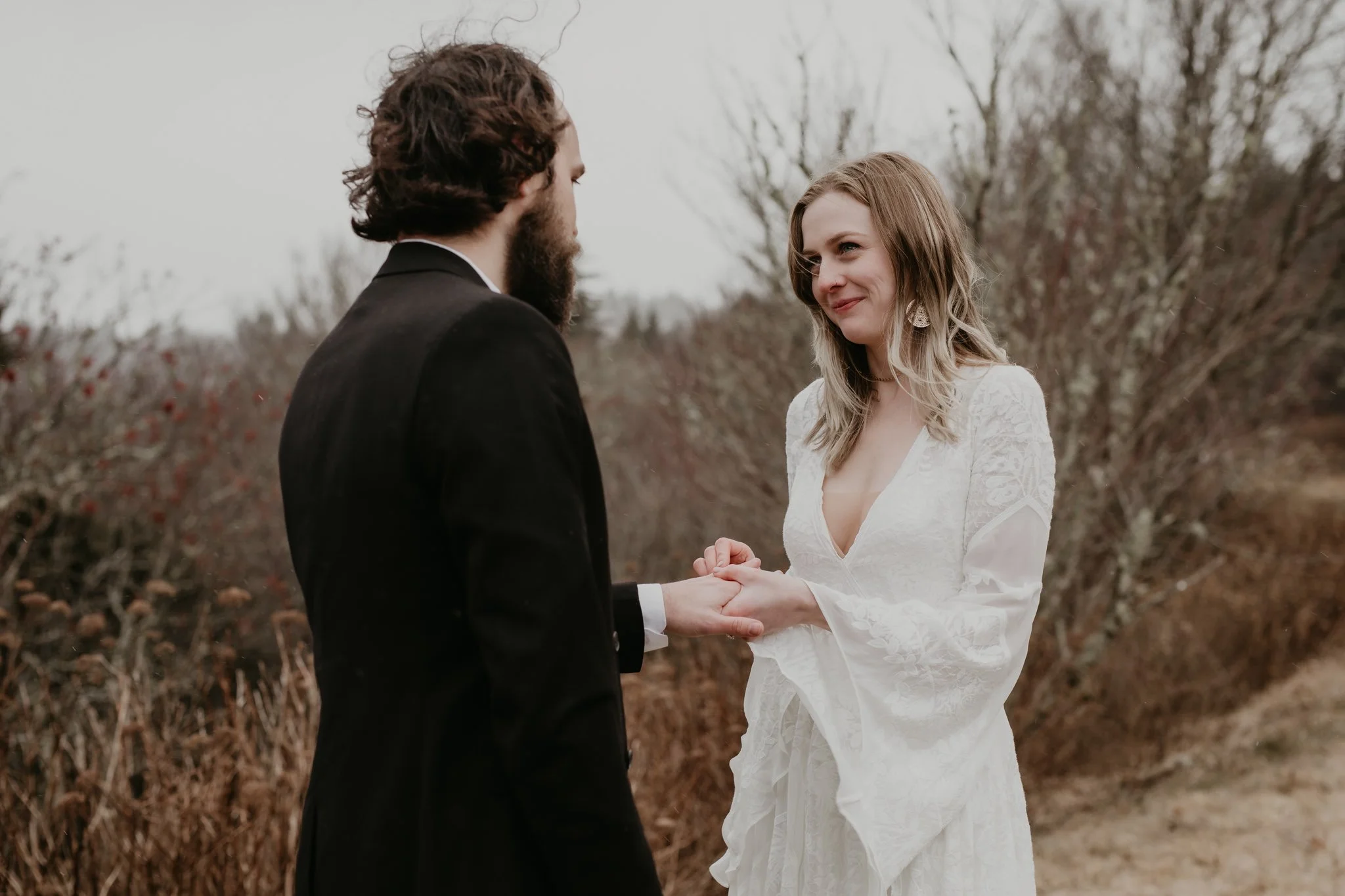 A bride places a ring on her grooms finger during a ceremony in a snowy Pisgah National Forest
