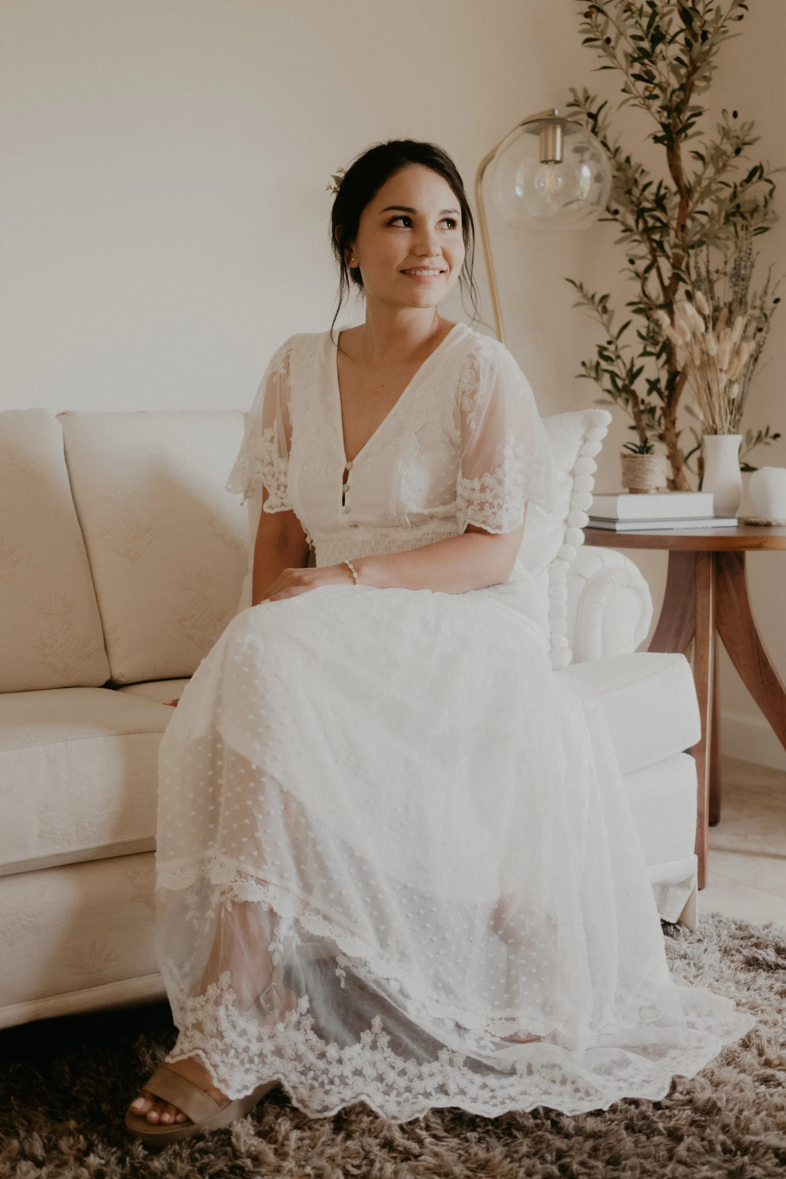 bride sits on her couch in her living room, light coming from the open window next to her