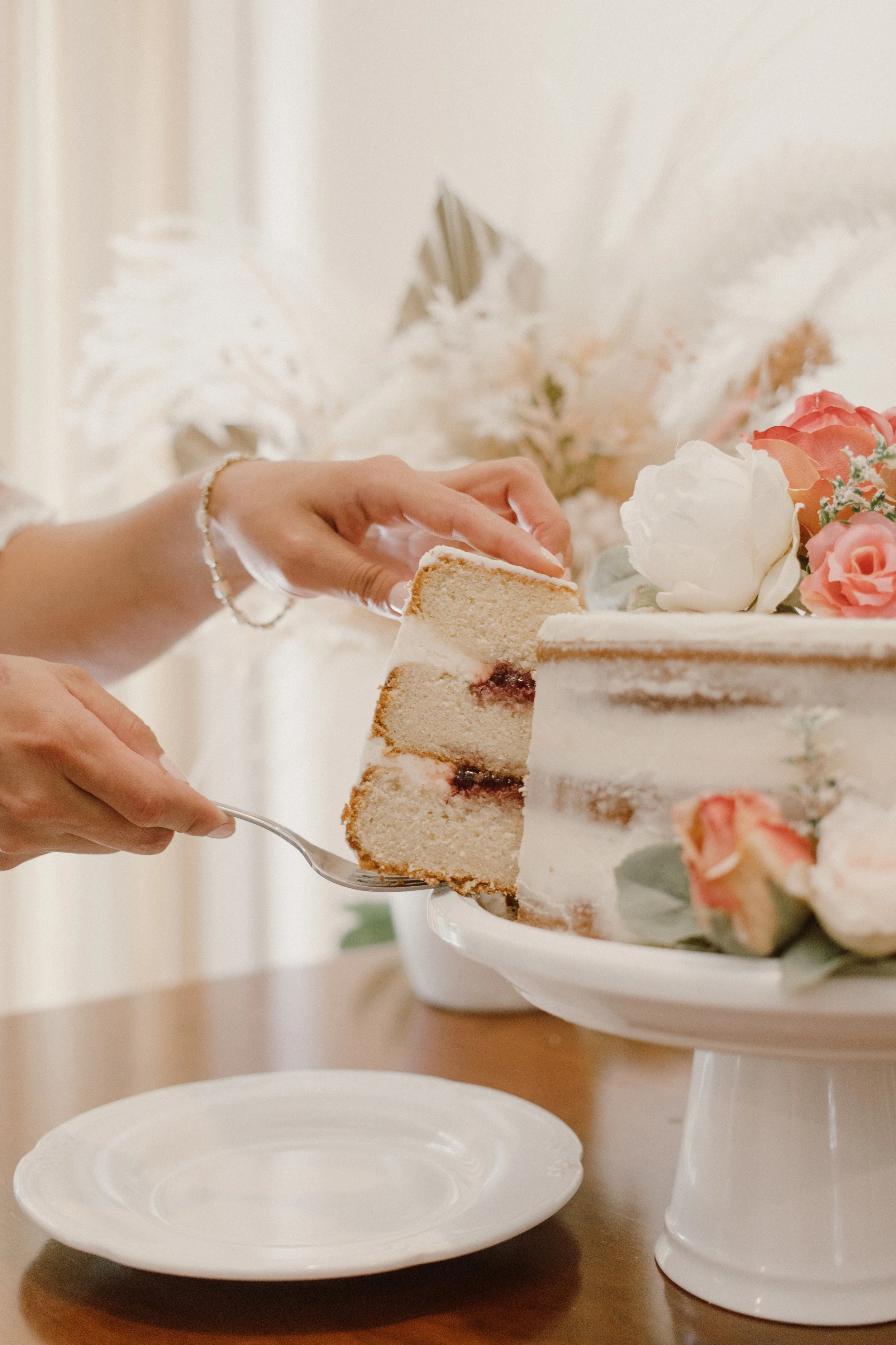 The bride reveals the cut piece of cake, with orange and white florals and dried palms used as decor.