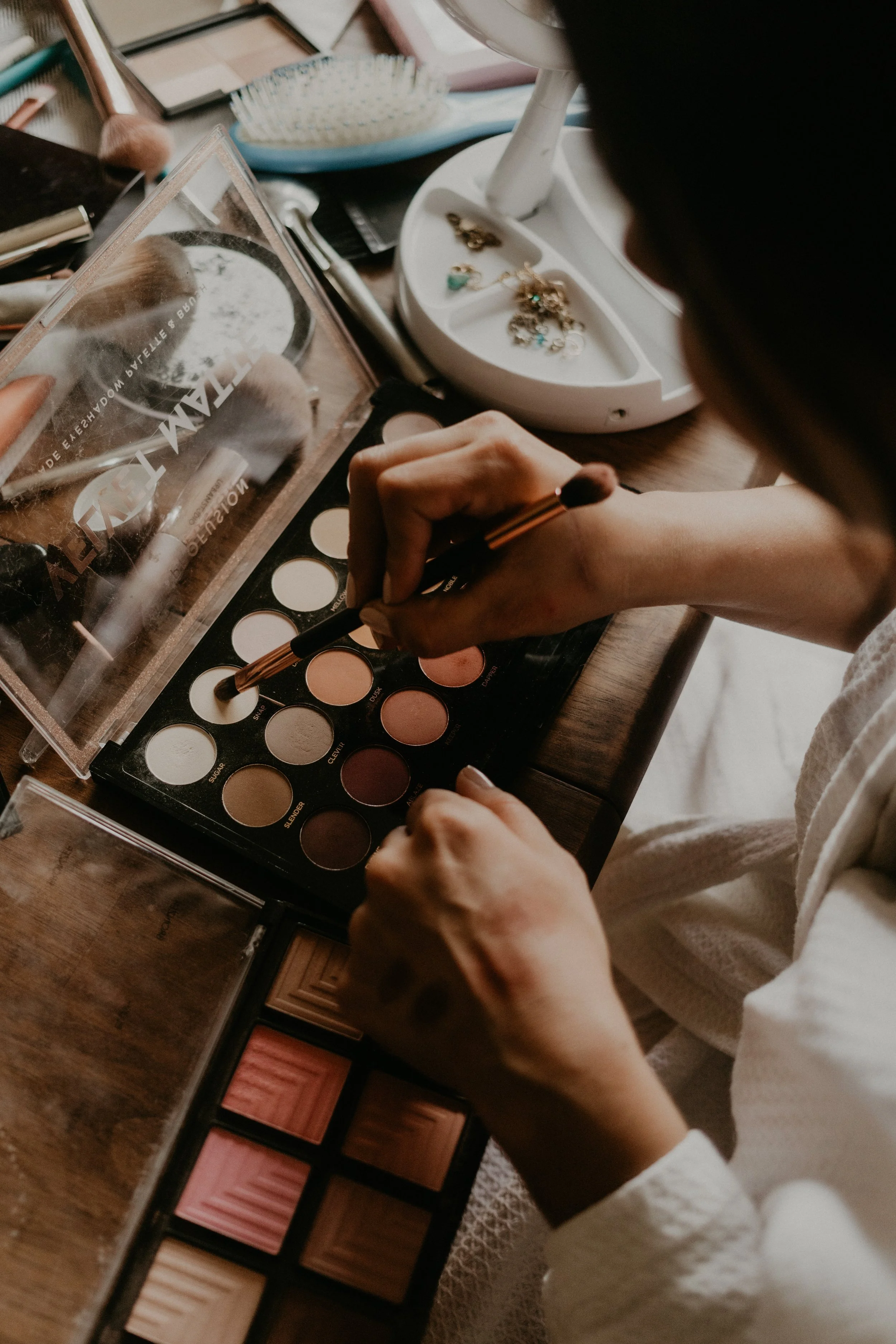 Above shot of makeup on a wooden table, a brush being dipped in eyeshadow