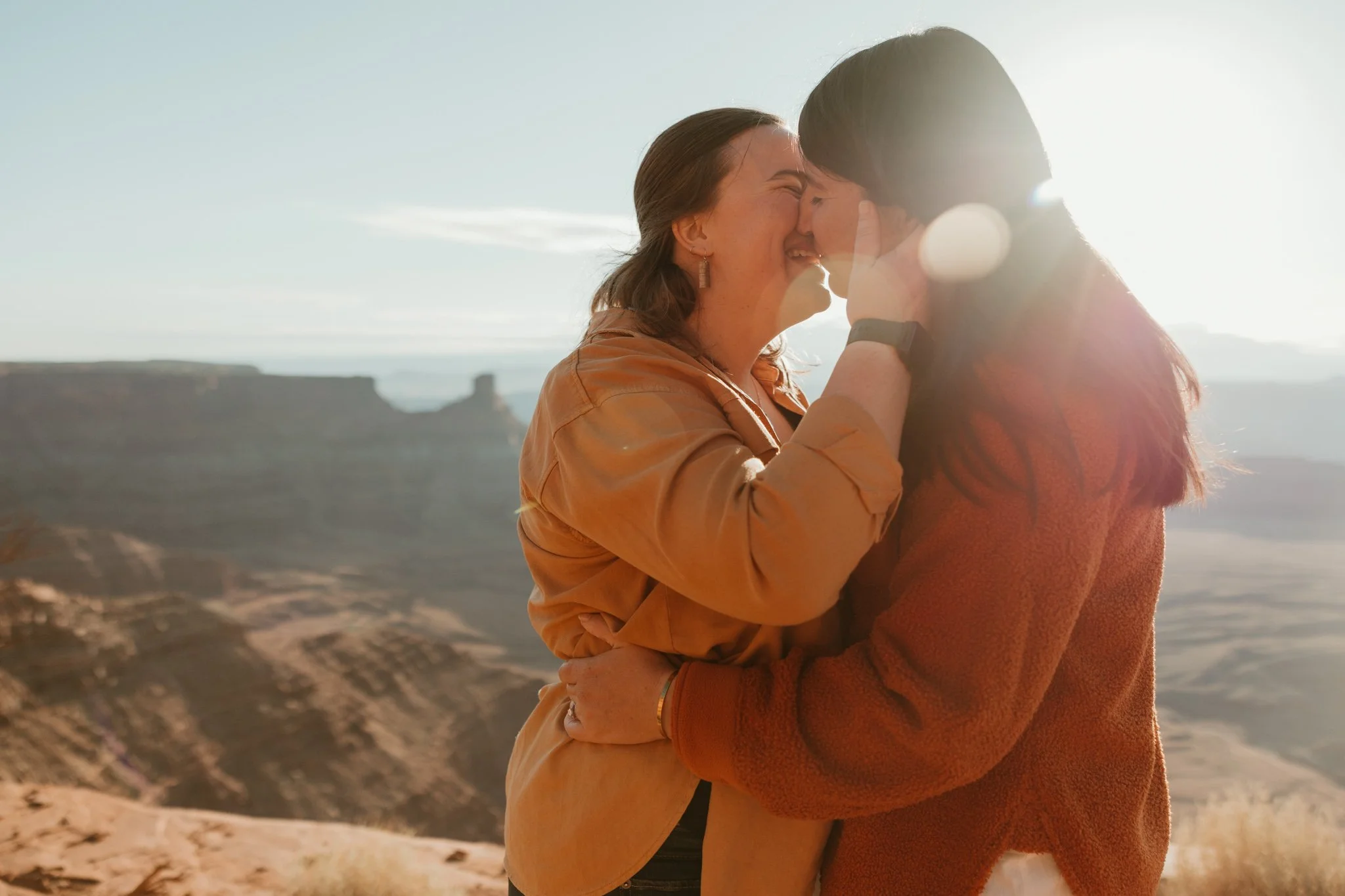 Queer couple going in for a kiss at sunrise during their engagement at Dead Horse Point State Park