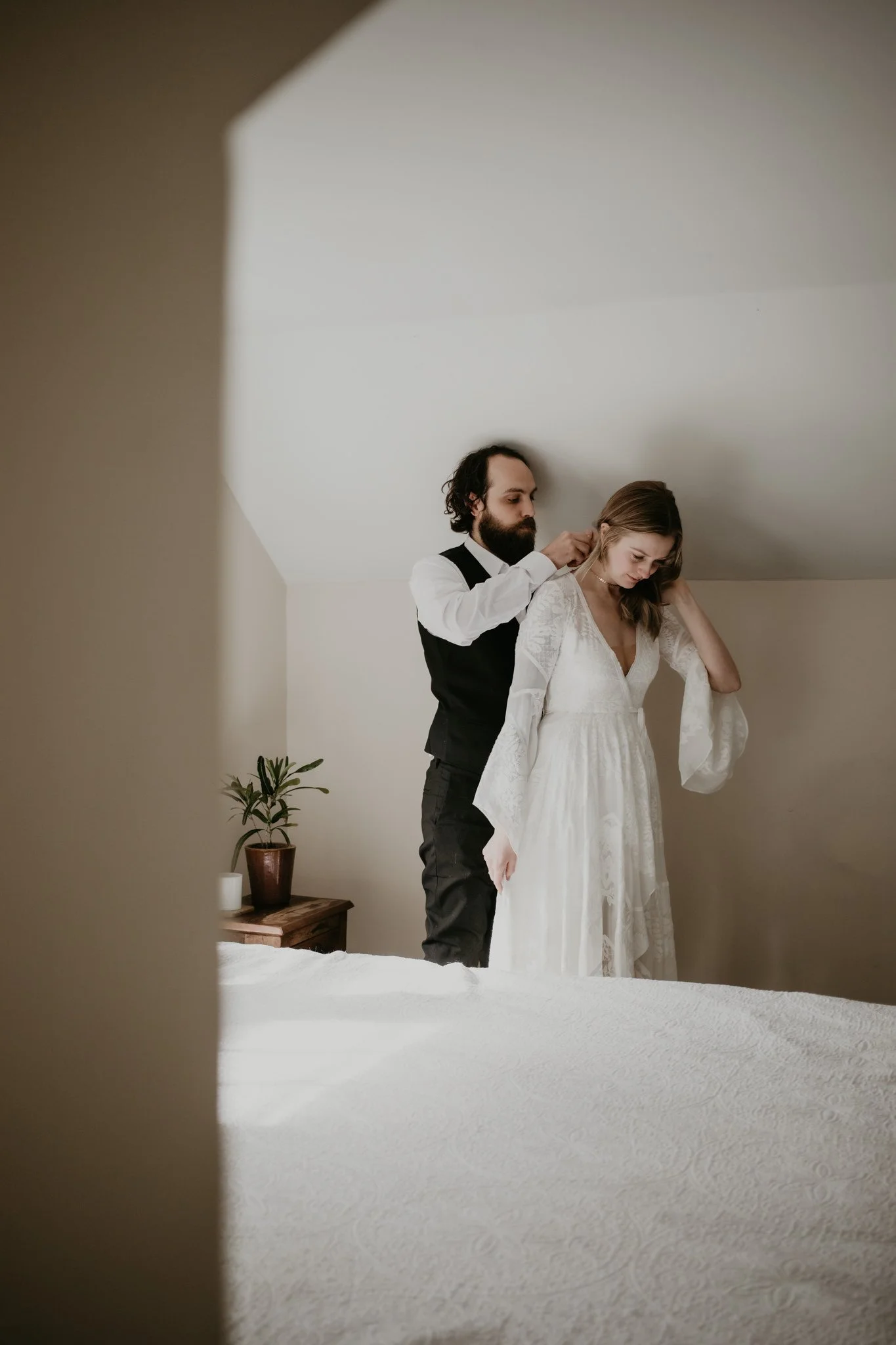 Elopement couple get ready together in their home with soft sun and moody shadows