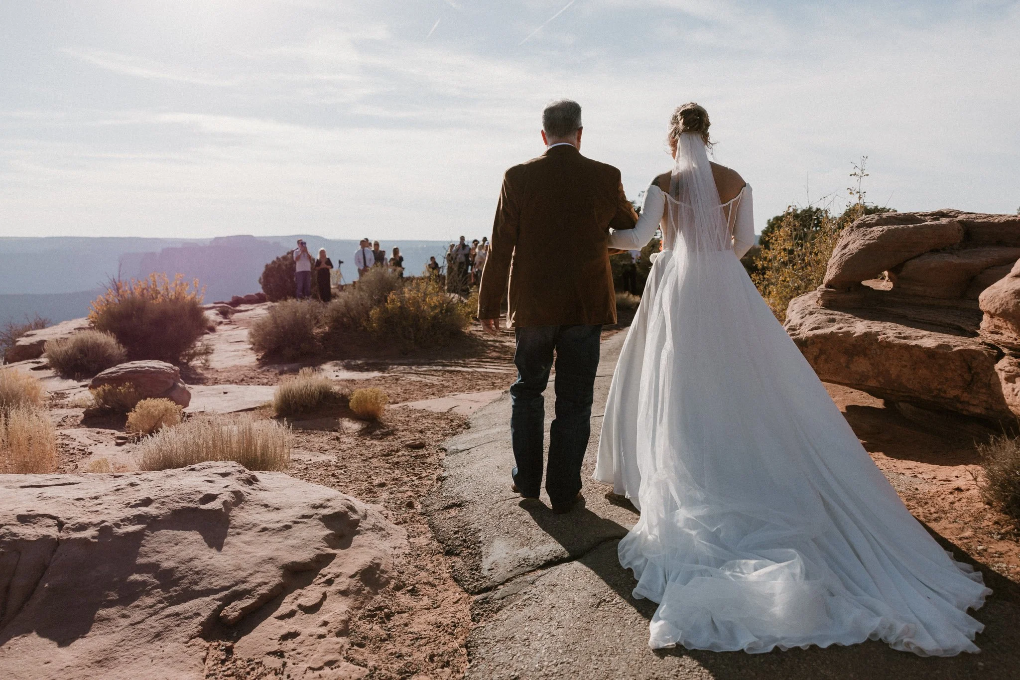 bride and her father walk down the paved path tot he west bench ceremony site at her intimate wedding in Dead Horse State Park
