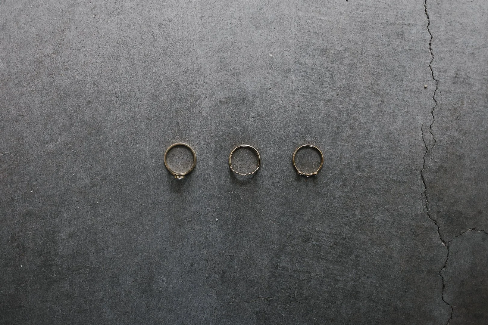 Three weddings rings arranged in a row on a dark gray concrete surface.