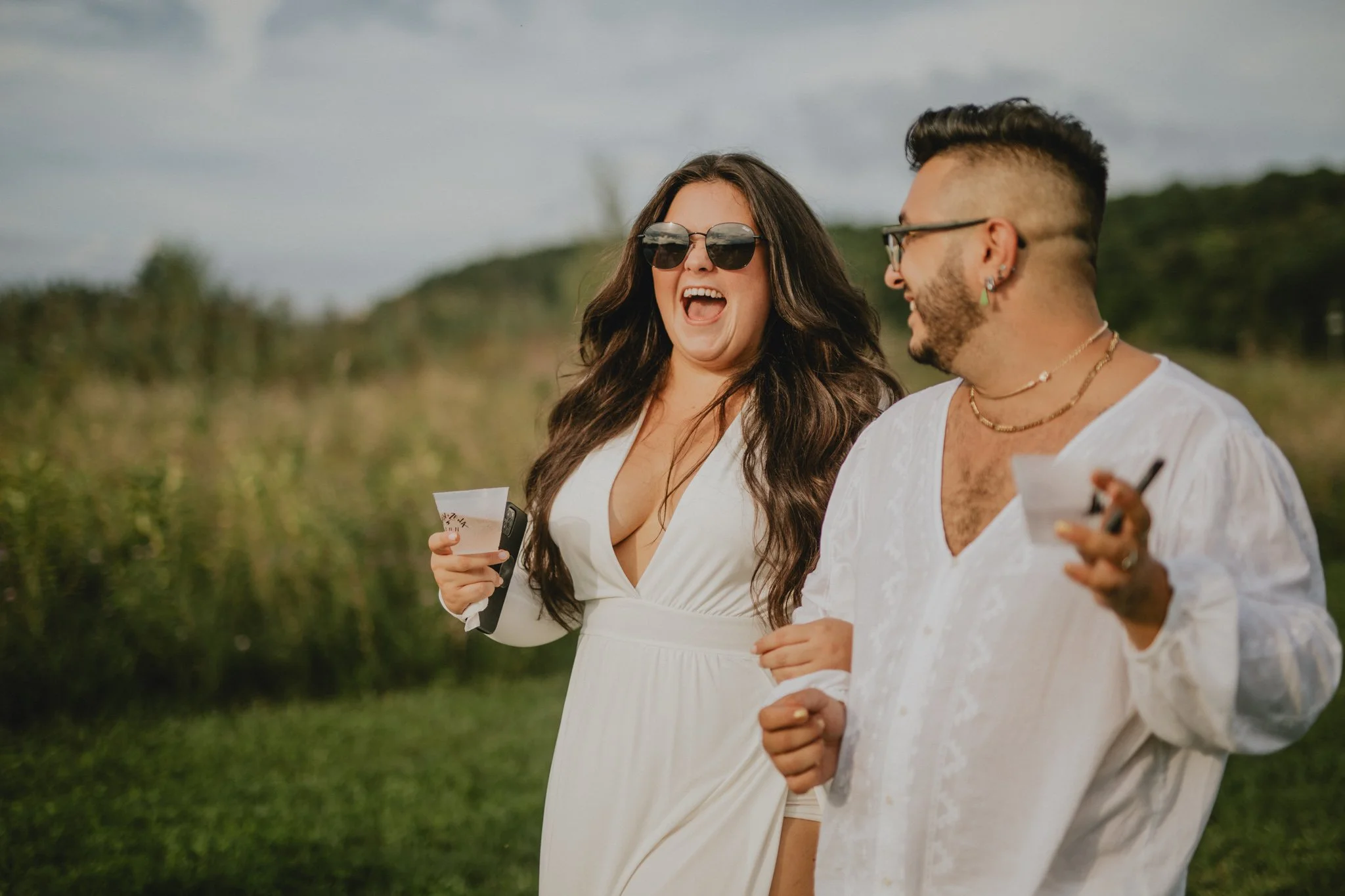 Two guests in all white walk towards the ceremony, with drinks in hand