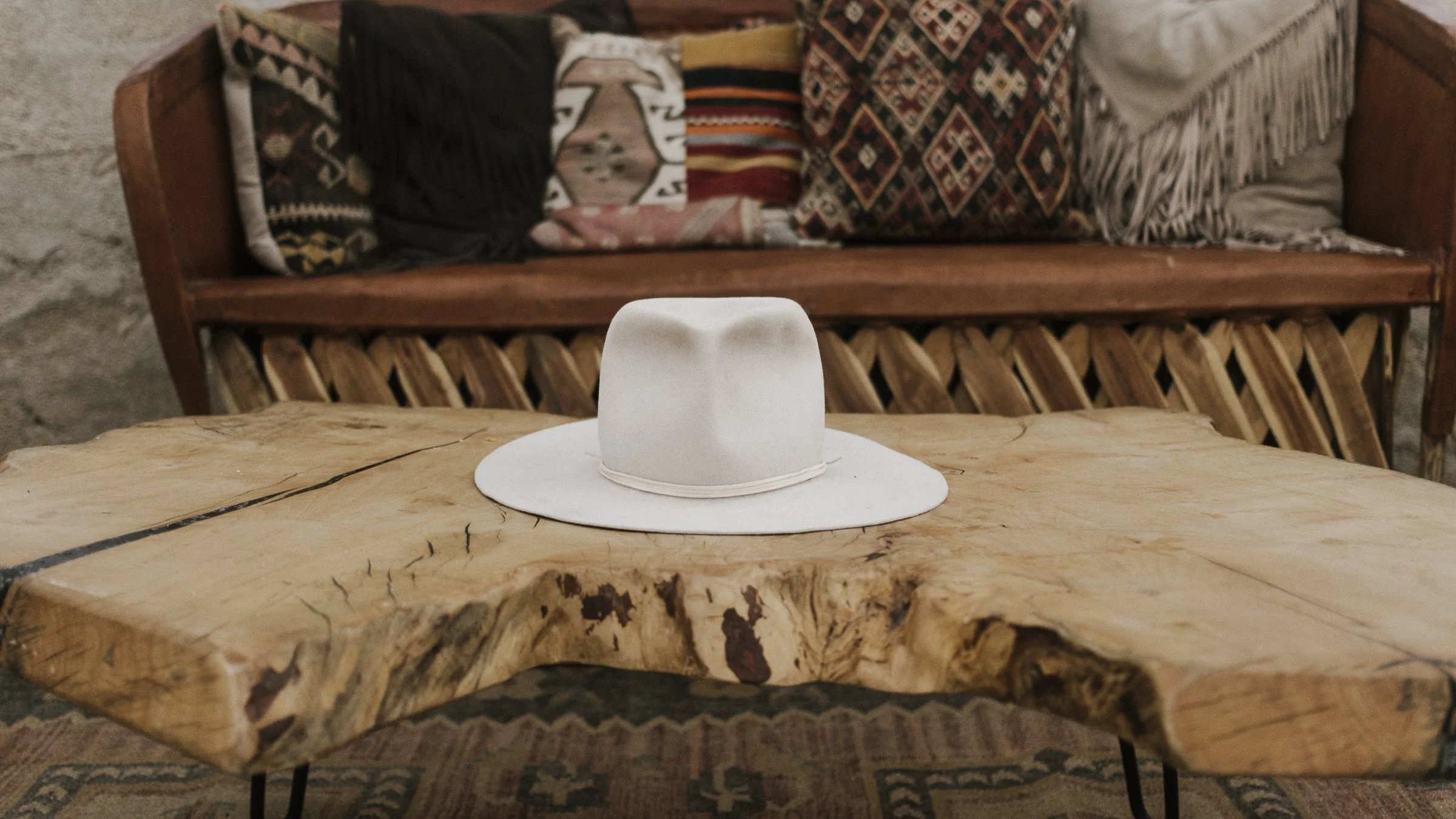 bridal cowgirl hat sits on a wooden table with a leather western inspired couch and pillows in the background
