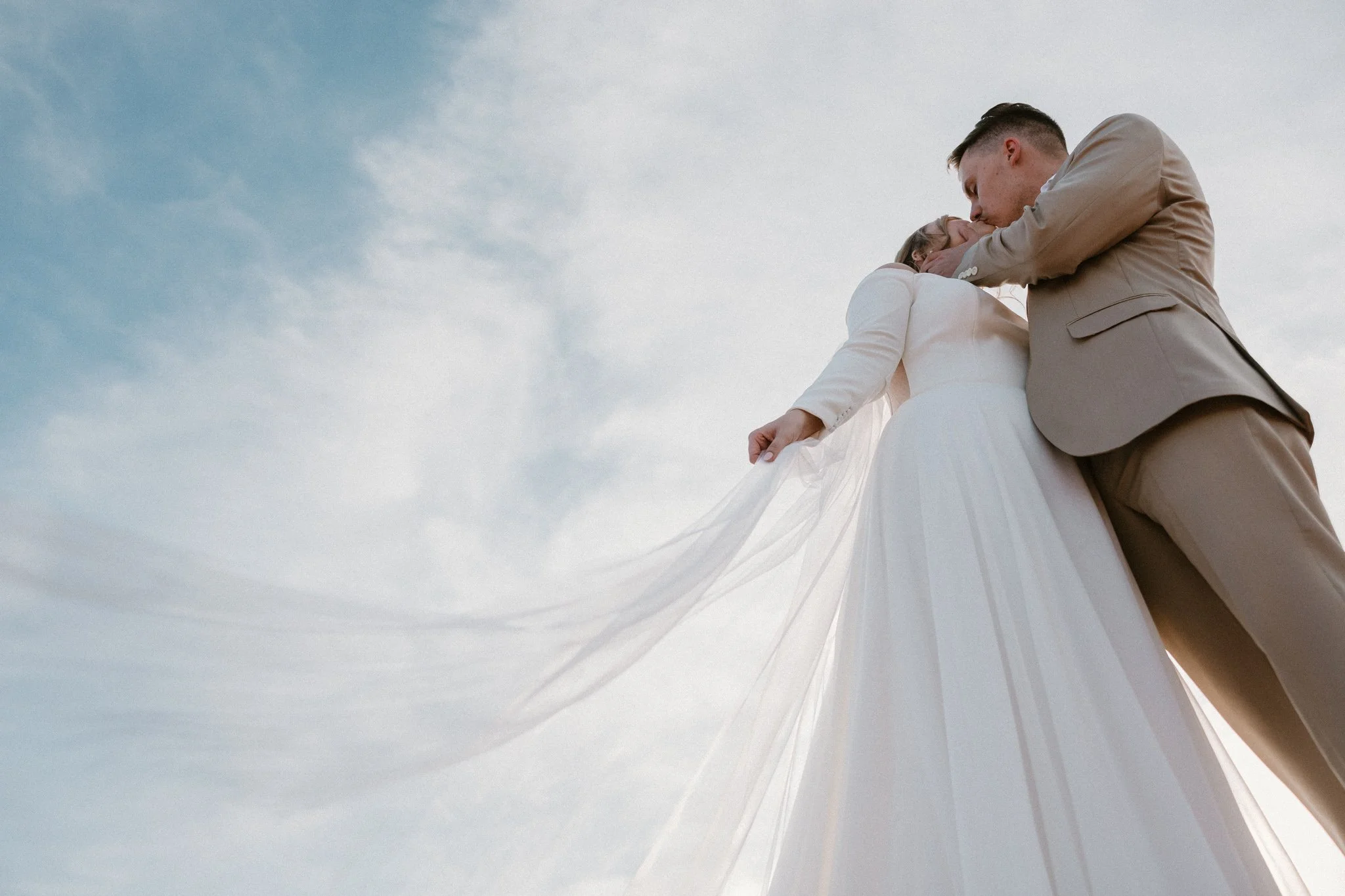 A bride and groom sharing a kiss at Dead Horse Point State Park with a cloudy sky in the background.