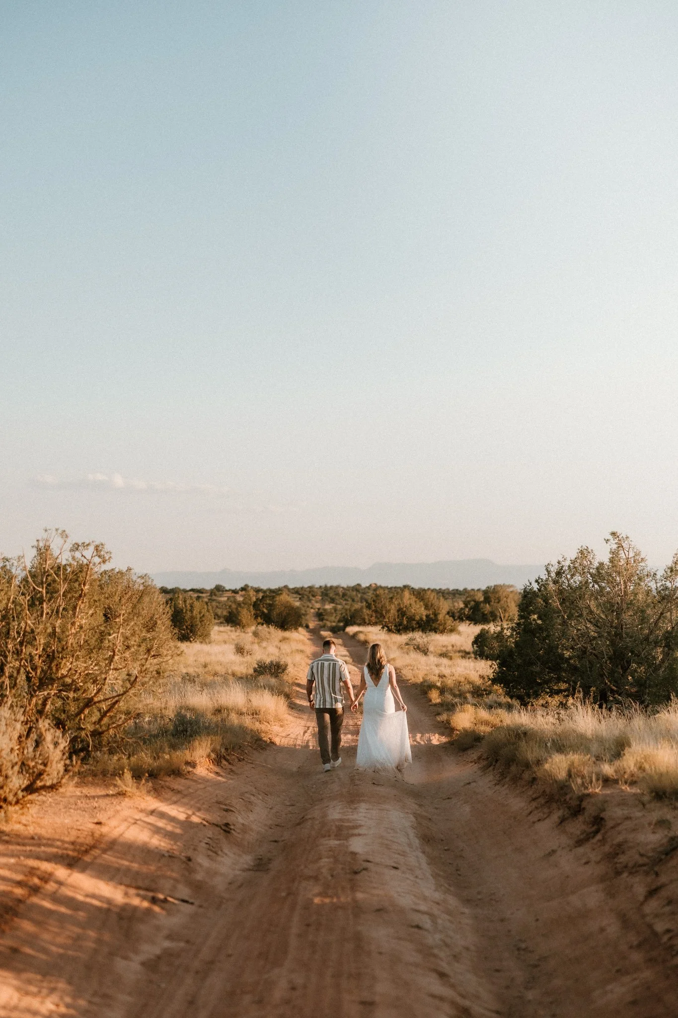 Tattooed couple walk along an off road path, holding hands, and celebrating their engagement in Dead Horse Point State Park