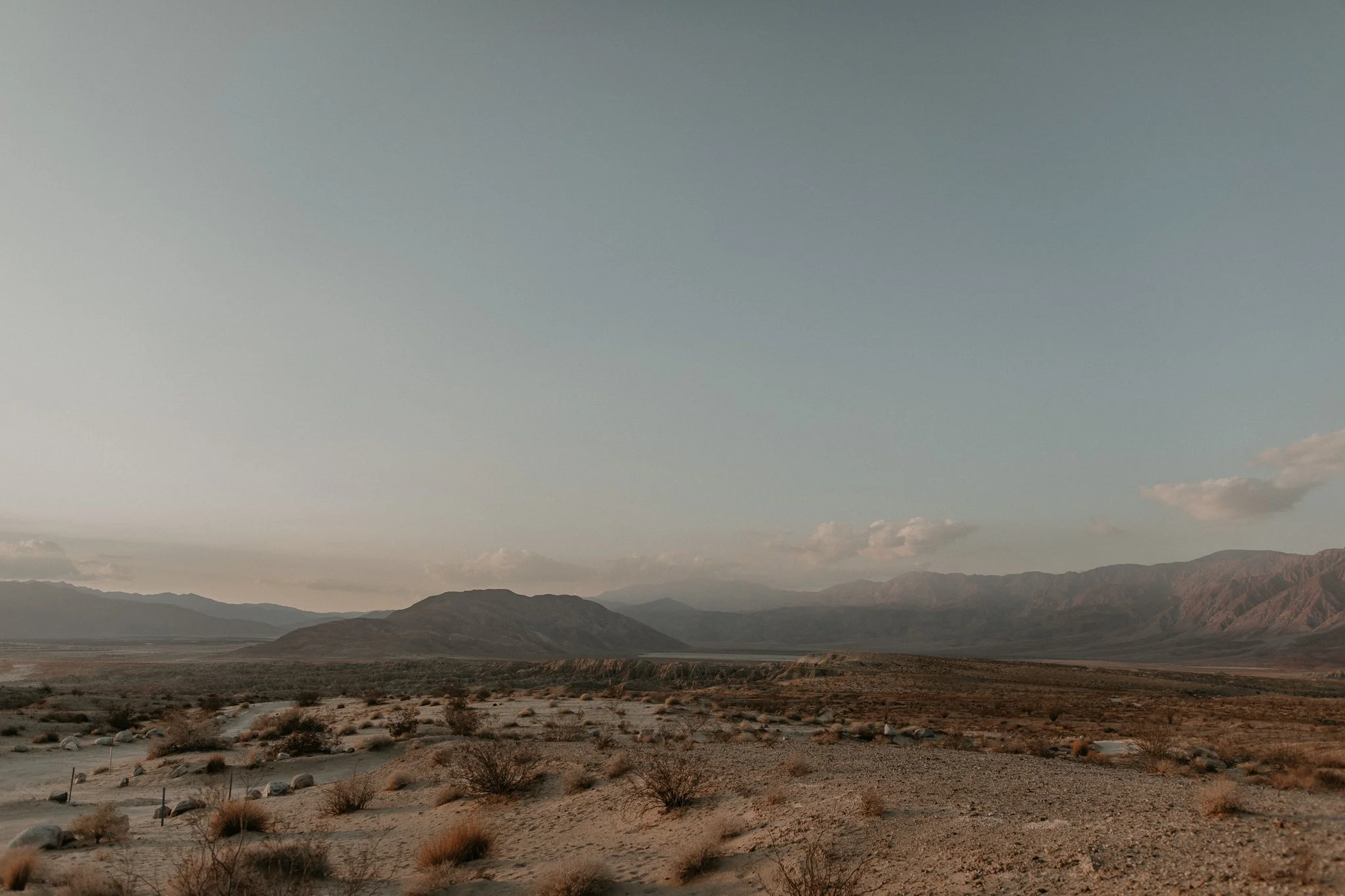 Desert landscape with scattered bushes, distant mountains, and a clear sky.