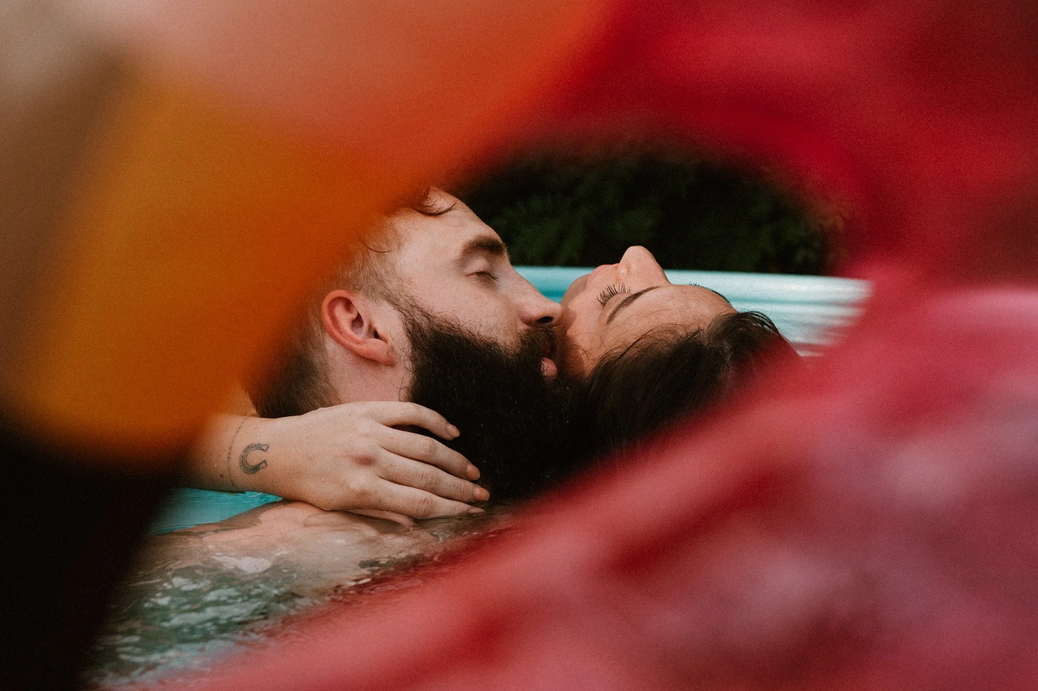 A close-up of a couple kissing while floating in a pool, surrounded by a flamingo float.