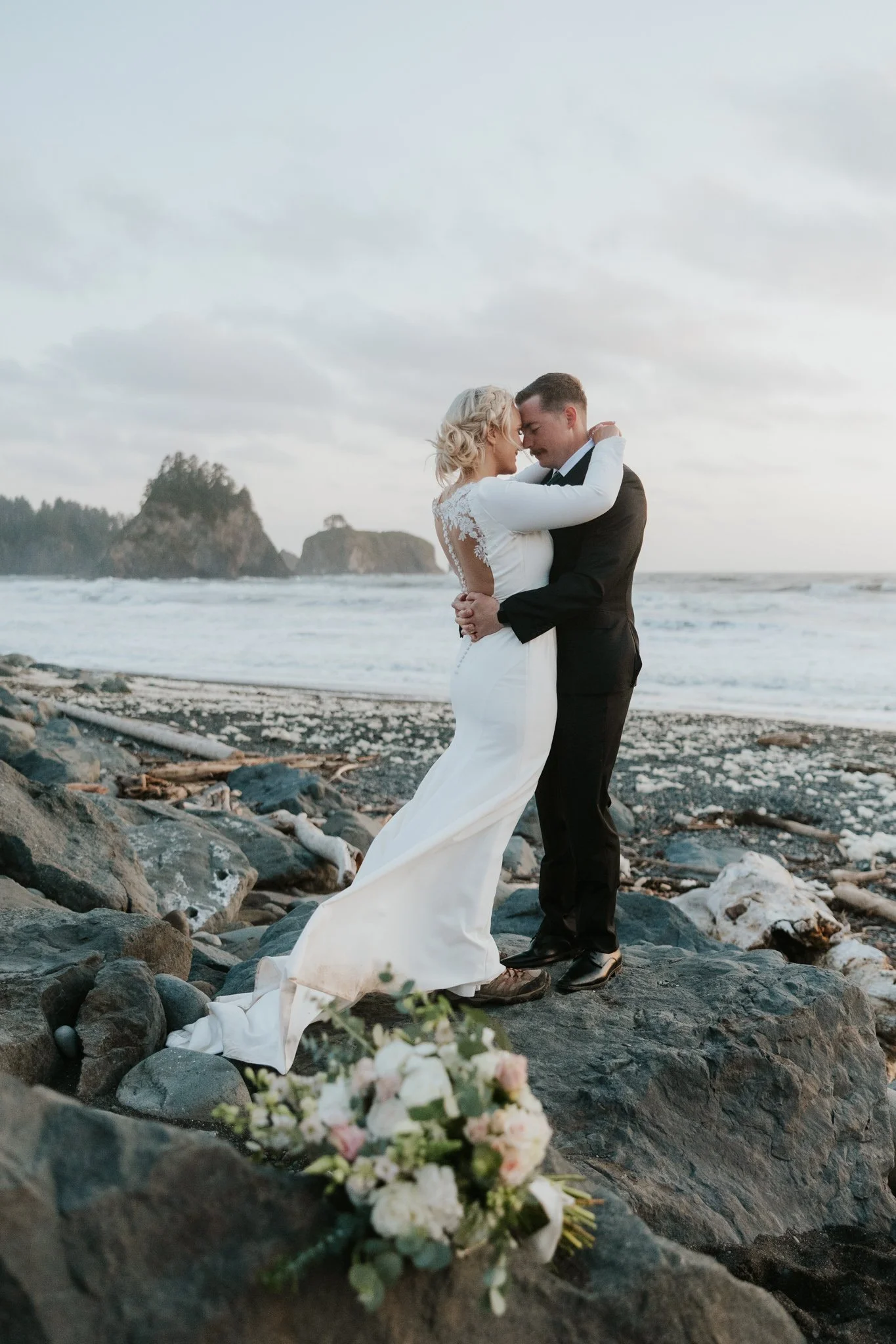 Wedding couple shares vows and embrace on the rocky coastline of Rialto Beach in Olympic NP