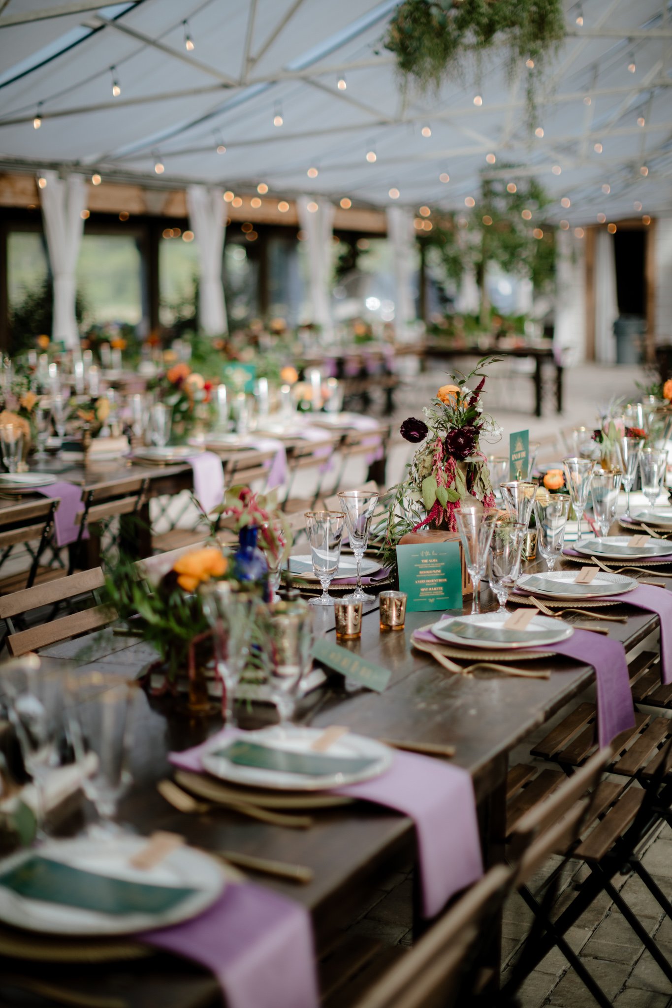 Long tables with purple napkins and place settings with gold rimmed glasses and florals along the table.