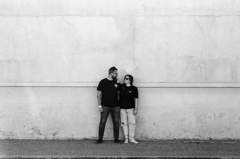 Paige and Corey of Going Home Co. standing close against a weathered concrete wall in Marfa, facing each other and smiling in black and white.