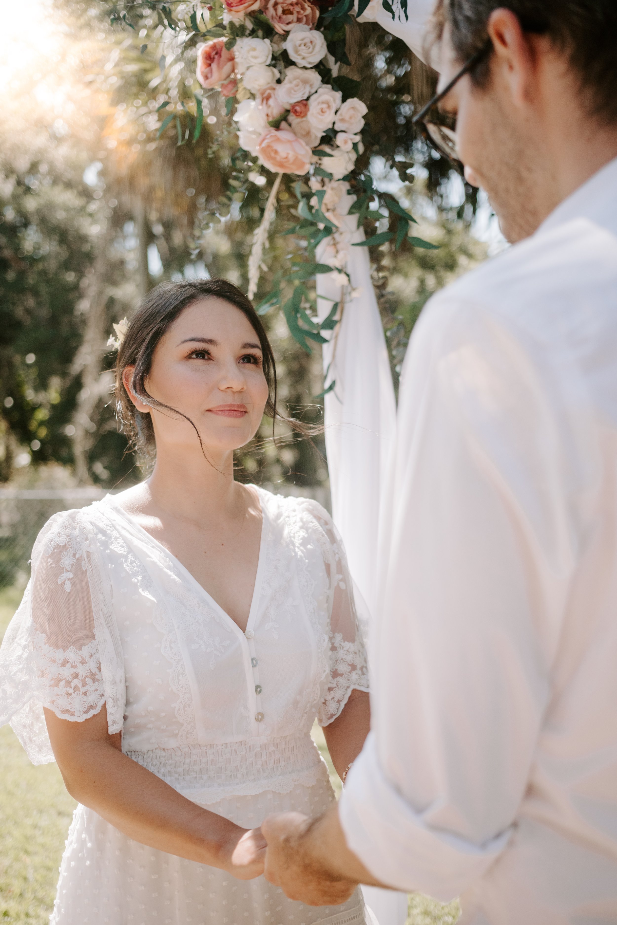 Bride looks up at her husband under and arch, with a the sun shining in the background.