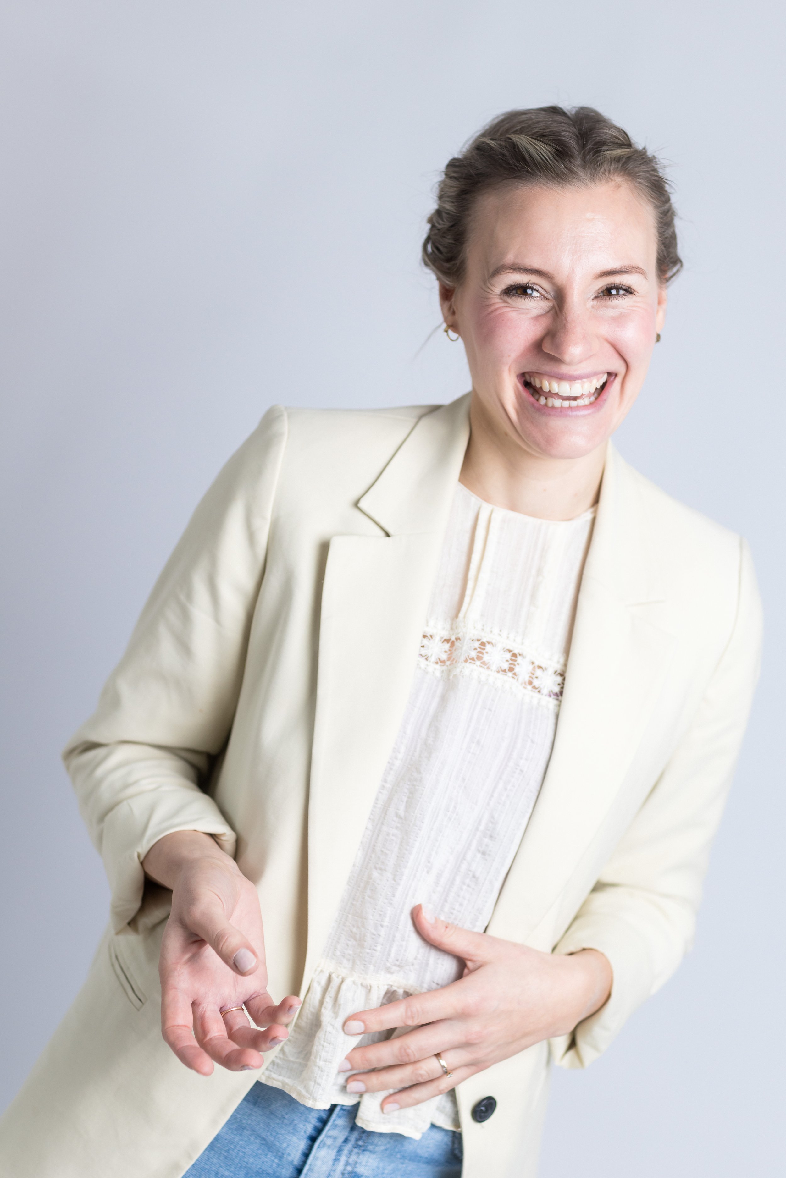 Lächelnde Frau in heller Jacke und Bluse, die mit ihrer Hand eine kleine Geste macht.