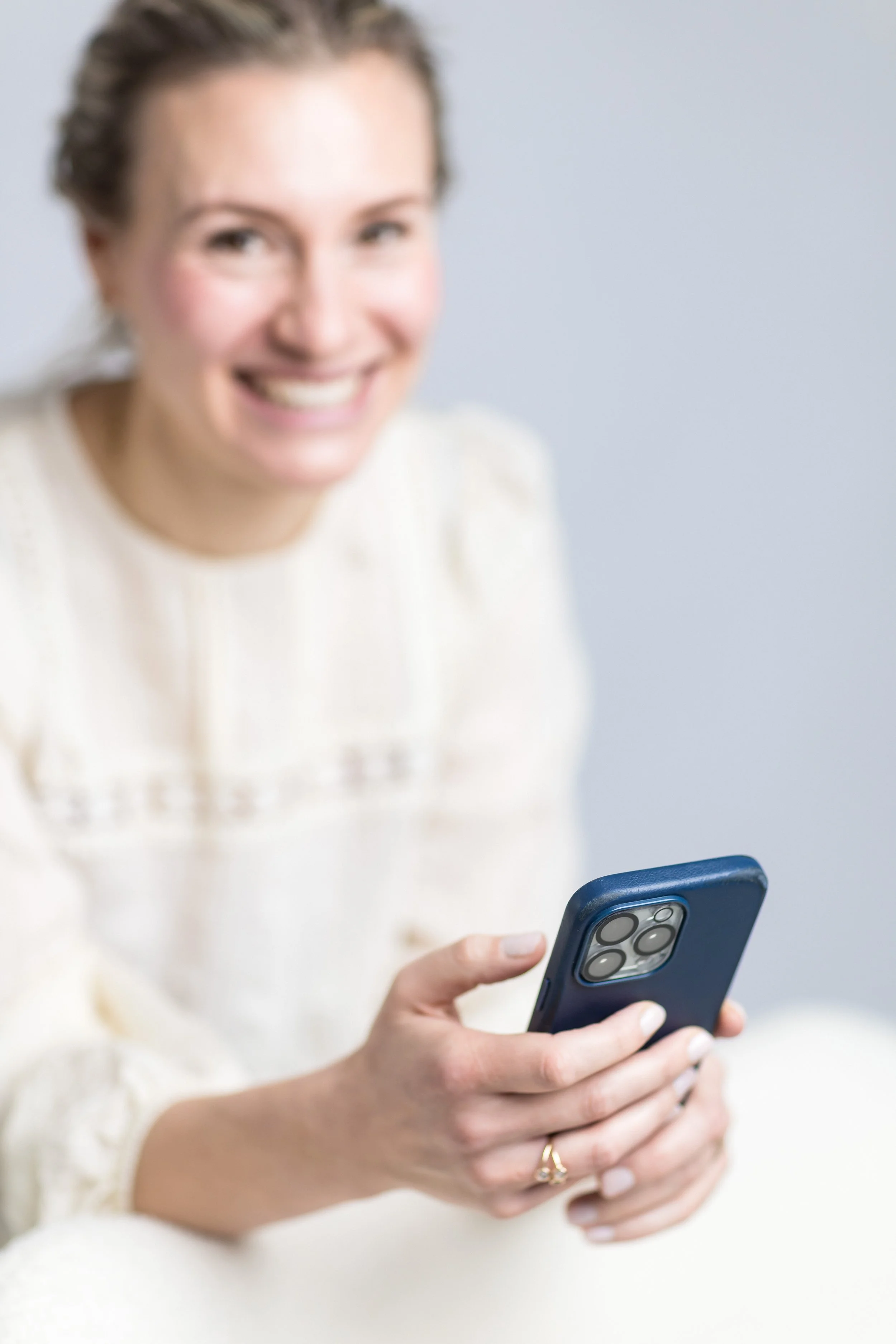 Eine lachende Frau hält ein Smartphone in der Hand, vor einem hellen Hintergrund.