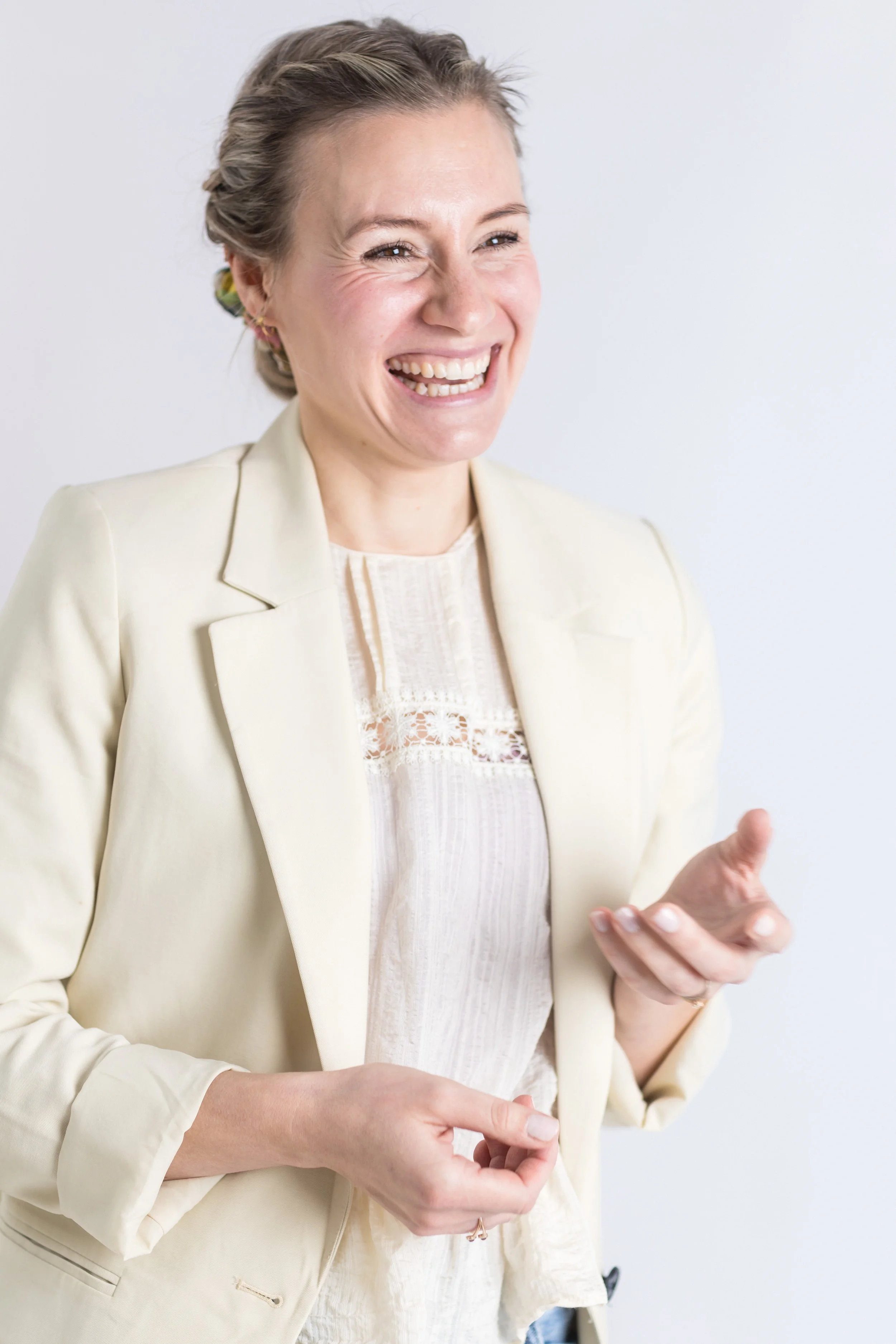Lächelnde Frau mit hellblauer Bluse und cremefarbener Jacke, die in einem Gespräch ist, vor weißem Hintergrund.