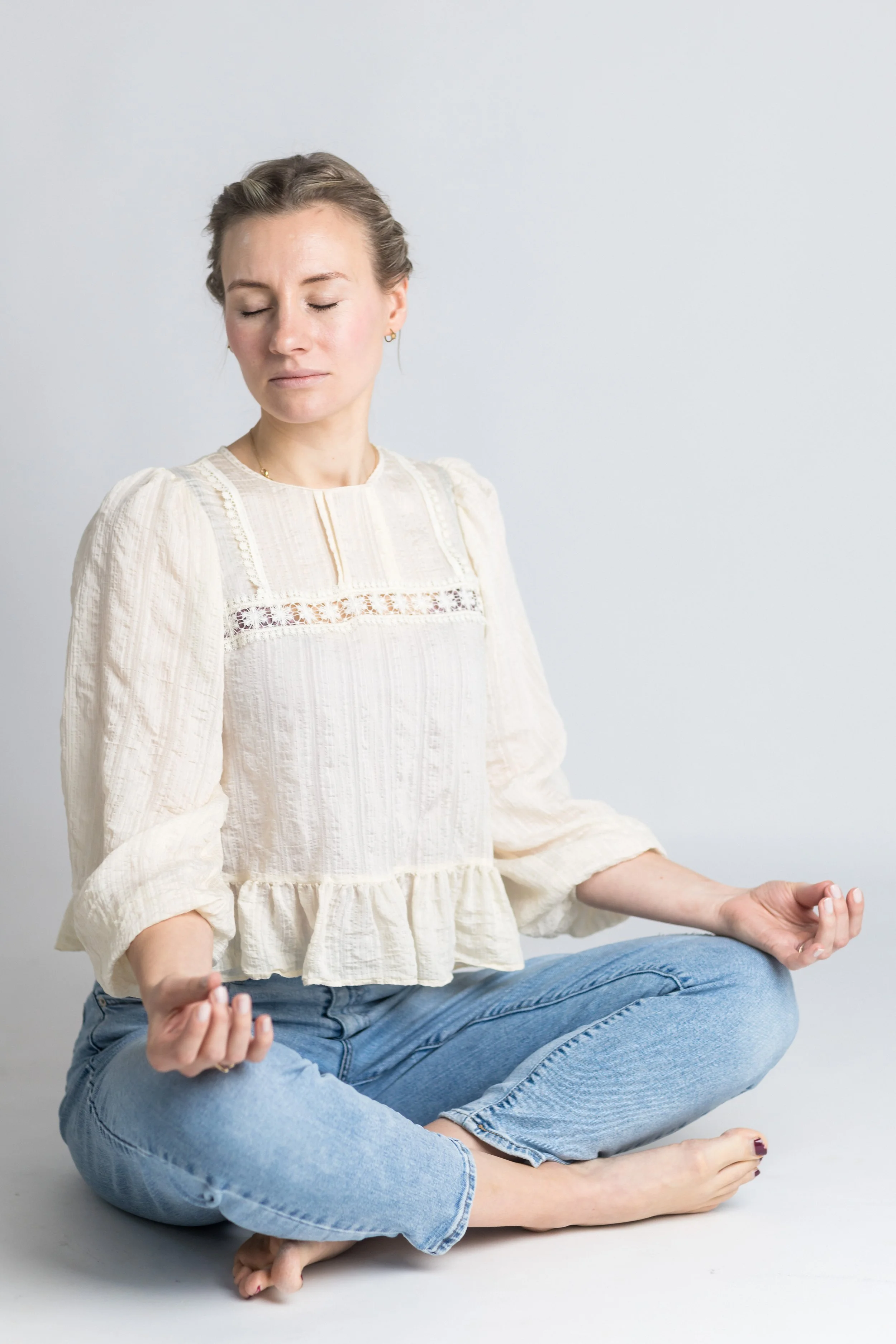 Eine Mama sitzt im Schneidersitz und meditiert mit geschlossenen Augen vor einem weißen Hintergrund.