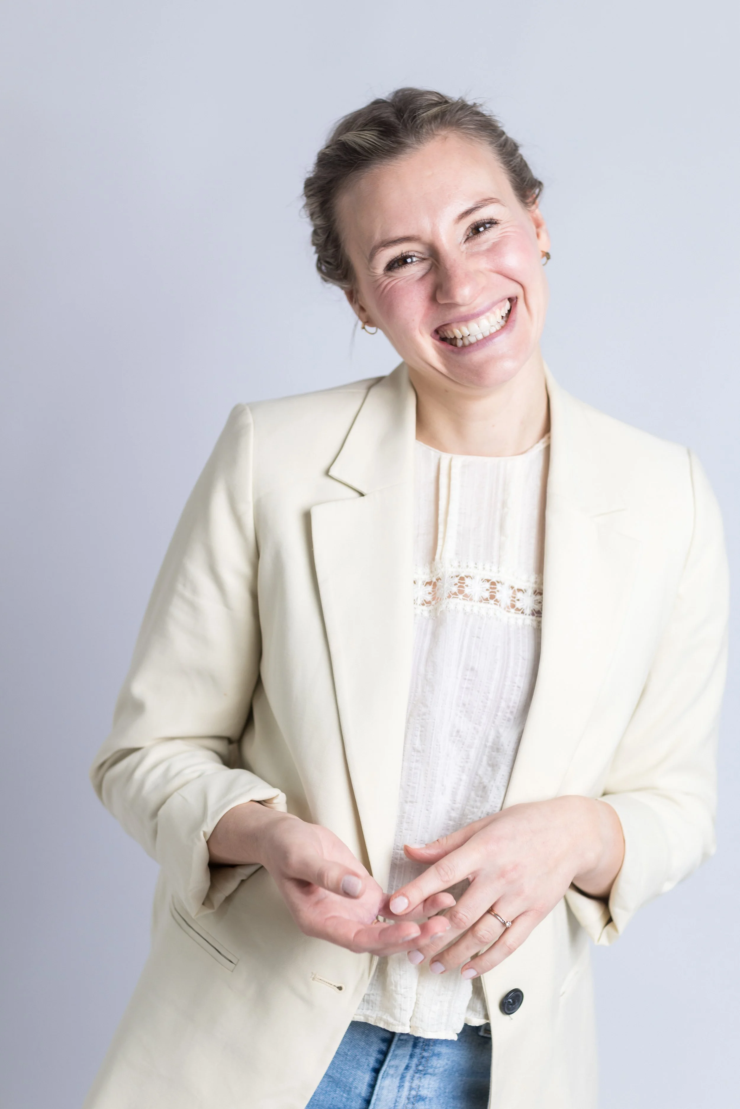 Lächelnde Mama in weißem Blazer und blauer Jeans vor hellem Hintergrund