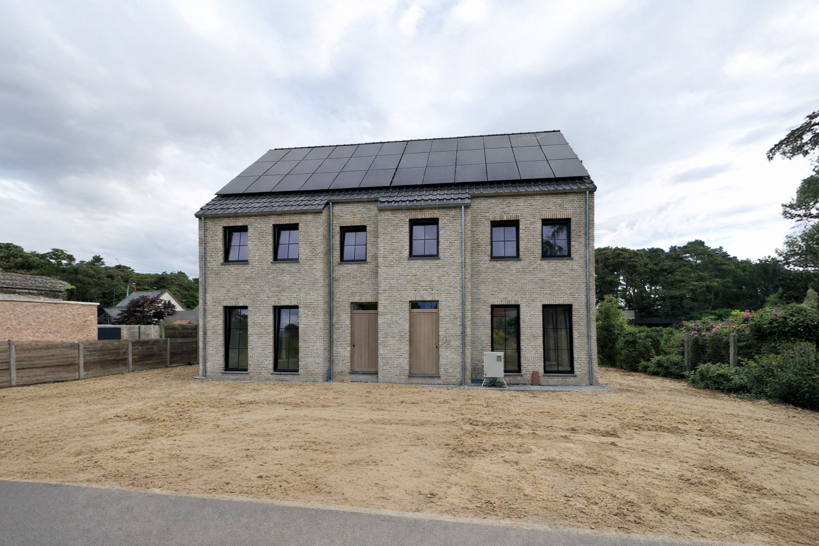 Nieuw gebouwd twee-onder-een-kap woning met zonnepanele op het dak, op een kavel met nog geen gazon, in een landelijke omgeving.